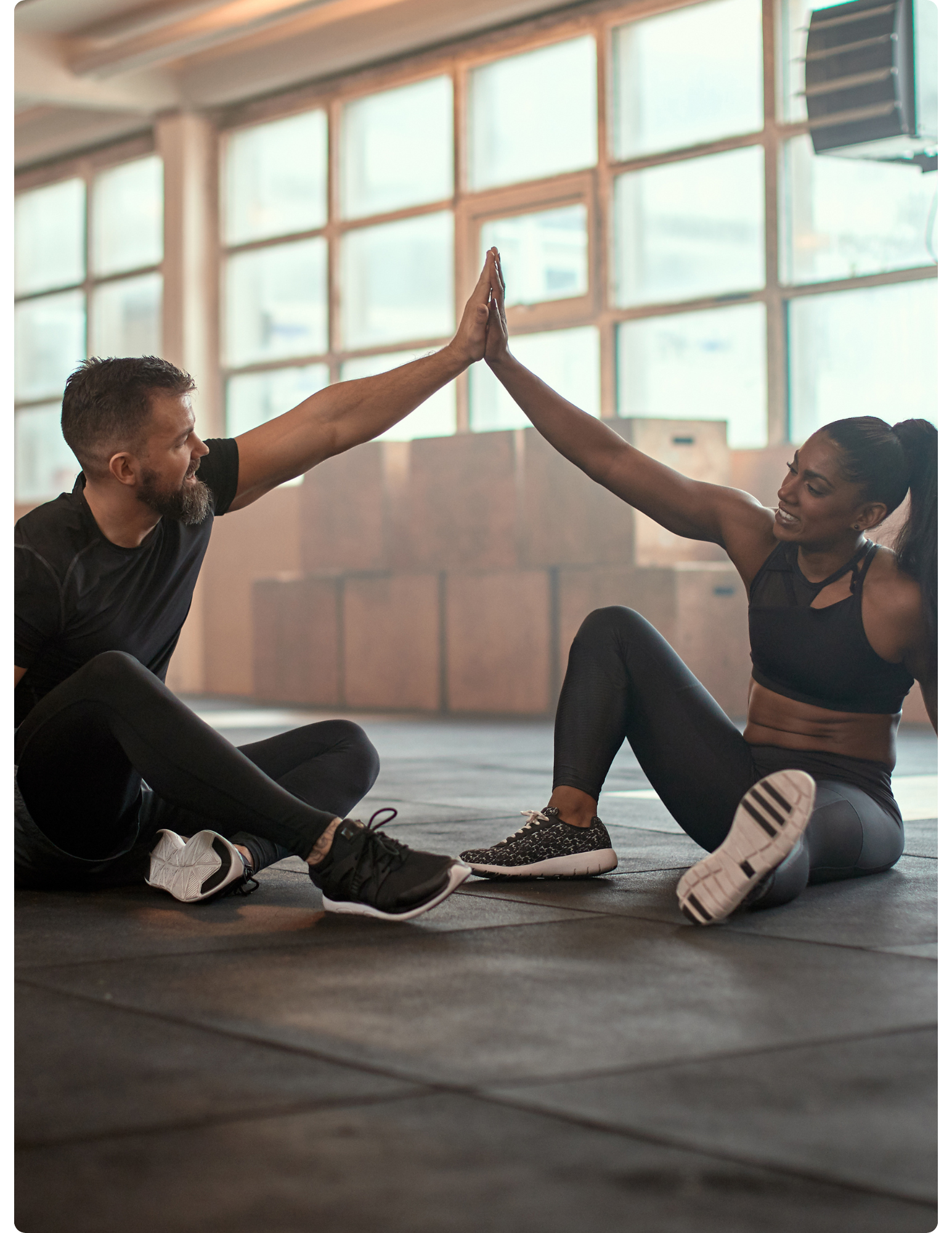 A man and woman sitting on gym floor giving each other a high five after workout.