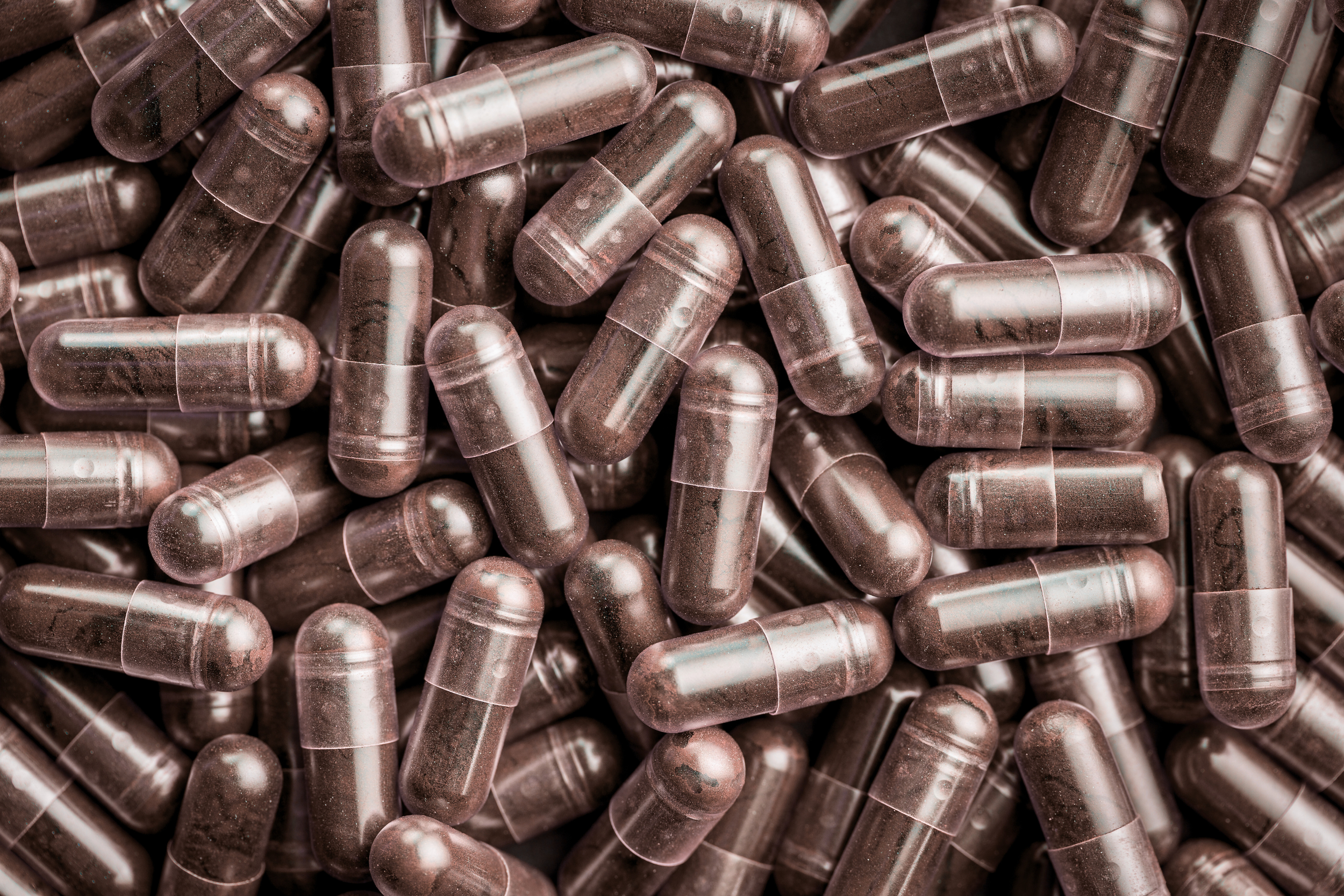 Close-up view of numerous red sorghum botanical extract capsules or pills with a semi-transparent outer shell.