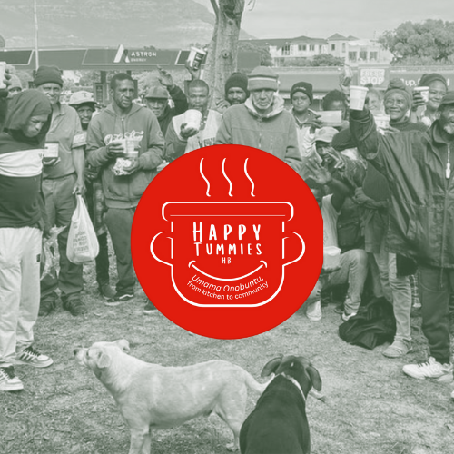 A group of people standing outdoors, some holding cups, with two dogs in the foreground. There is a large red circle graphic with a steaming bowl icon and the words "Happy Tummies" in the center. The background includes trees, commercial buildings, and a street.
