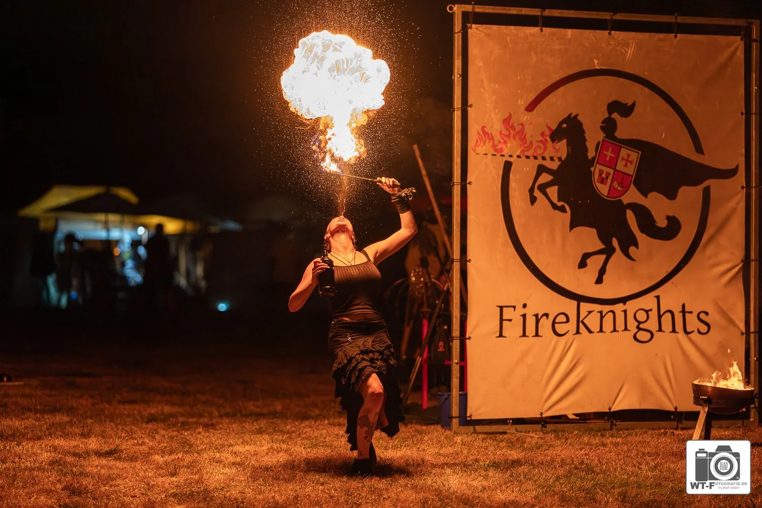 Eine Frau führt eine Feuershow bei Nacht auf einem Festival namens Fireknights auf, während sie Feuer speit und eine Flamme in die Luft schleudert