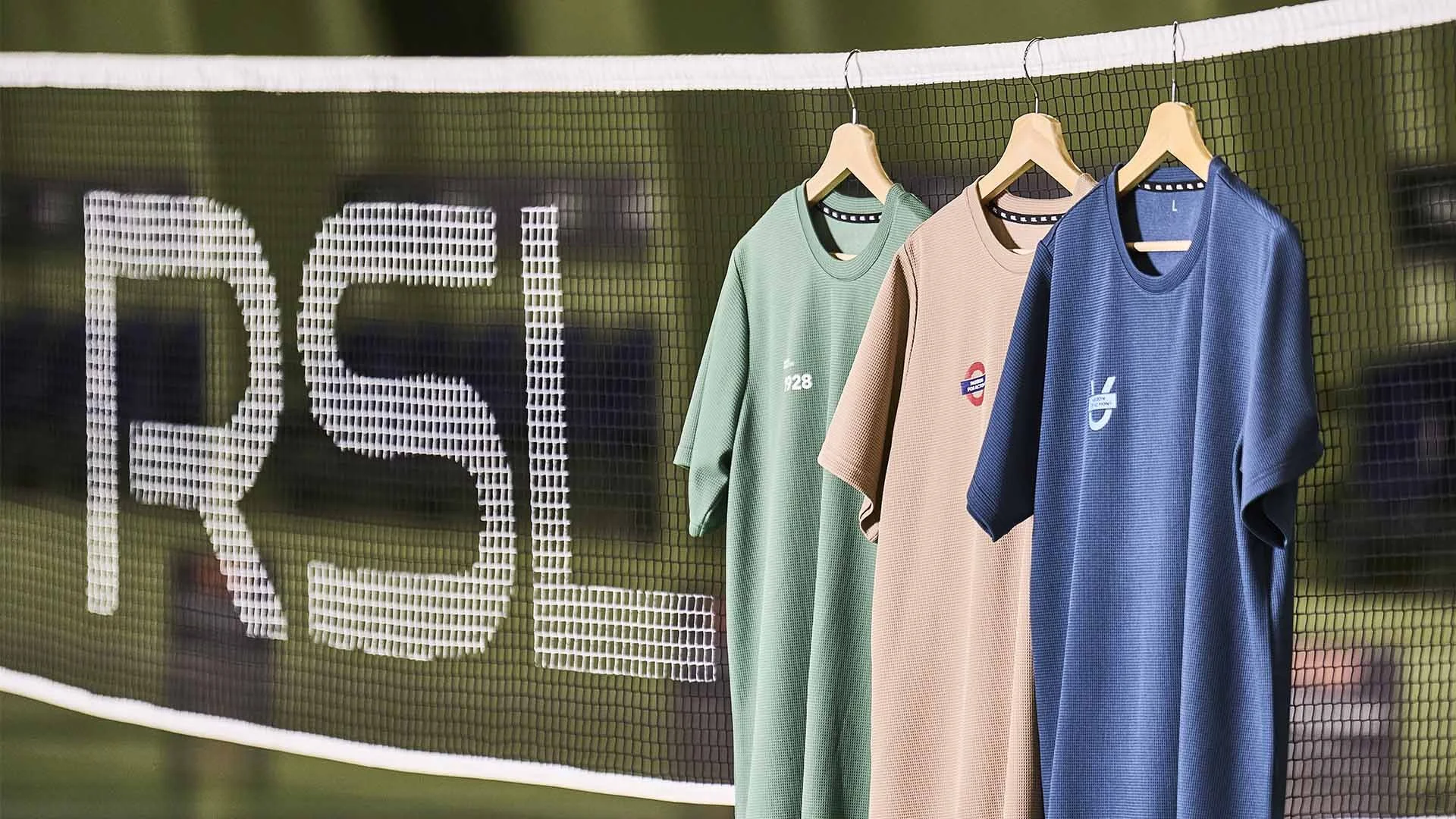 Tre farverige sports T-shirts hænger på bærestænger foran en volleyballnet.