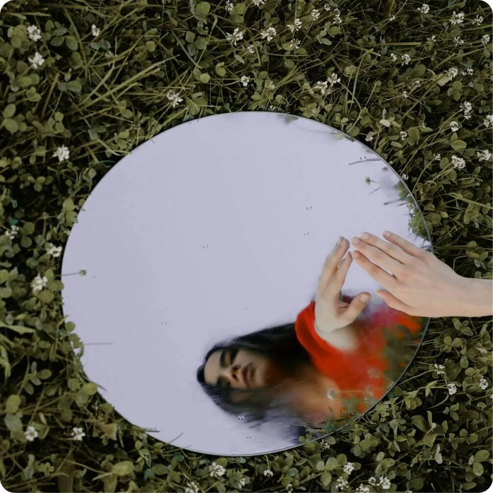 Woman reflected in a mirror outdoors, illustrating self-reflection in holistic therapy.
