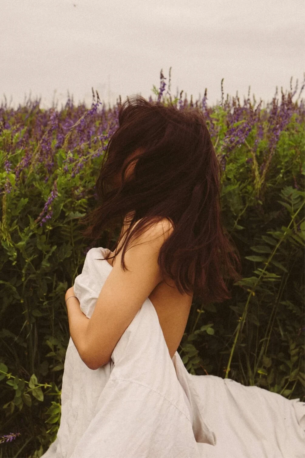 Woman embracing herself among flowers, illustrating self-compassion in holistic therapy.