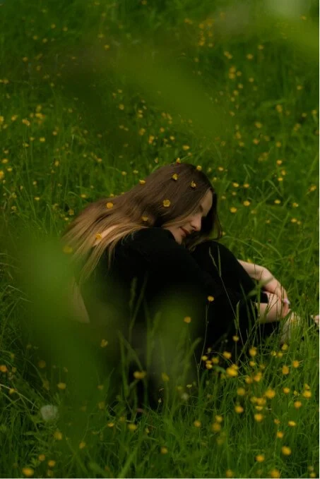 Woman sitting quietly in a meadow, illustrating reflection and emotional wellbeing in anxiety therapy.