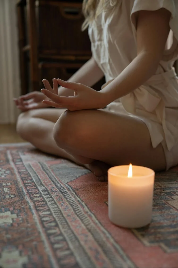 Woman meditating beside a candle, illustrating grounding and emotional regulation in trauma therapy.