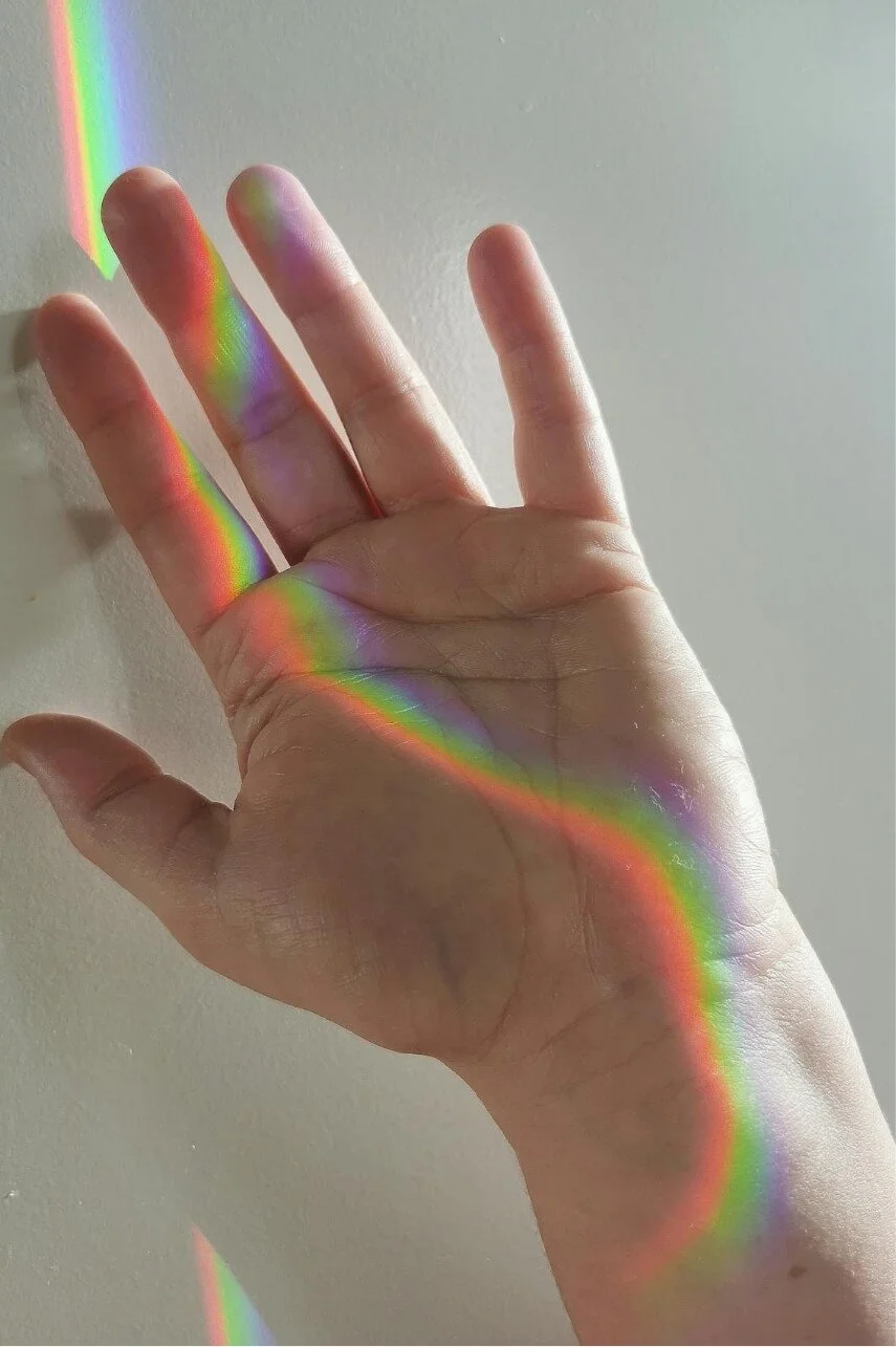 Hand illuminated by rainbow light, symbolizing mind-body connection in holistic therapy.