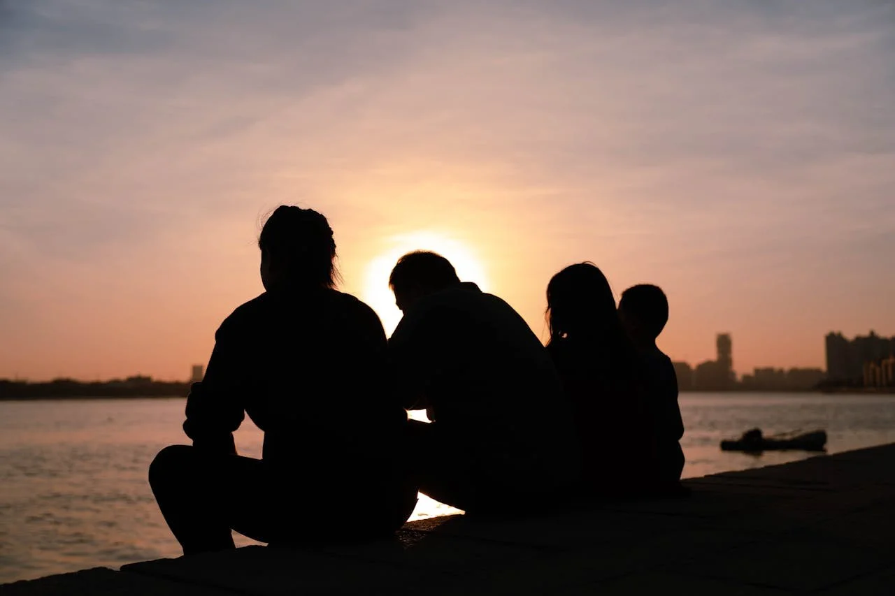 Family sitting together by the water at sunset, representing couples and family therapy in Switzerland.