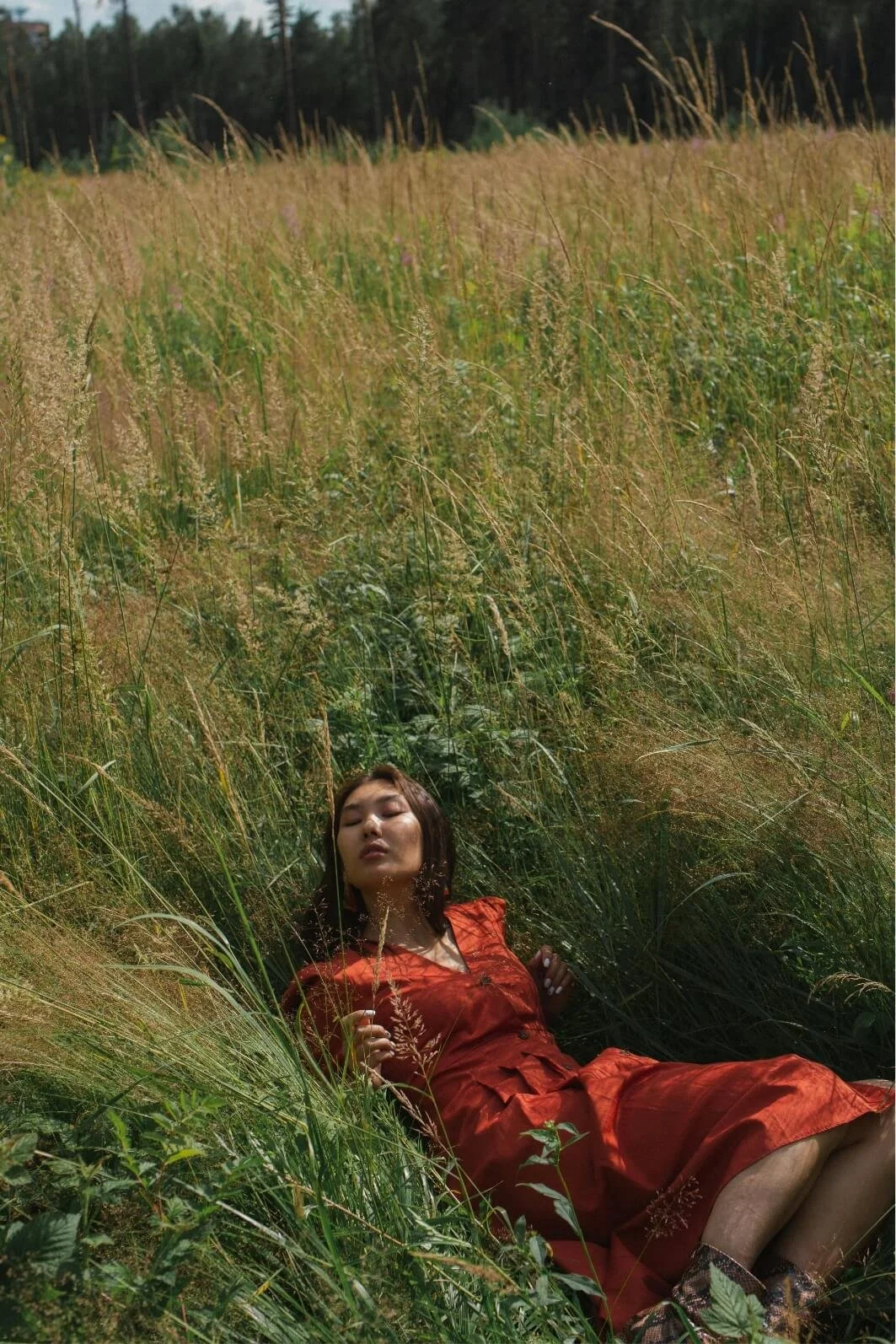 Woman resting in tall grass, illustrating rest, grounding and recovery in trauma therapy.