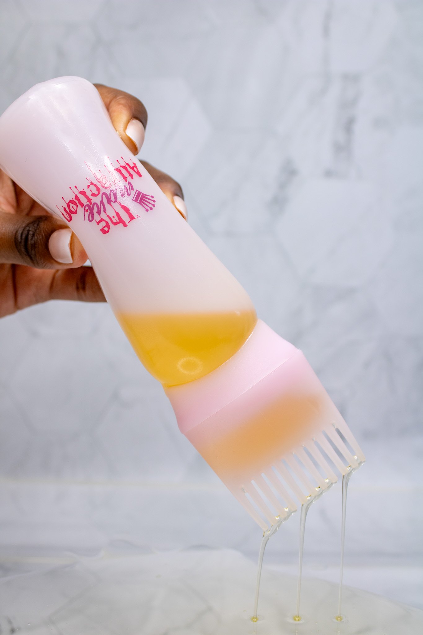 A hand holds a pink and white silicone menstrual cup tilted upside down, with yellow menstrual fluid dripping from its tips.