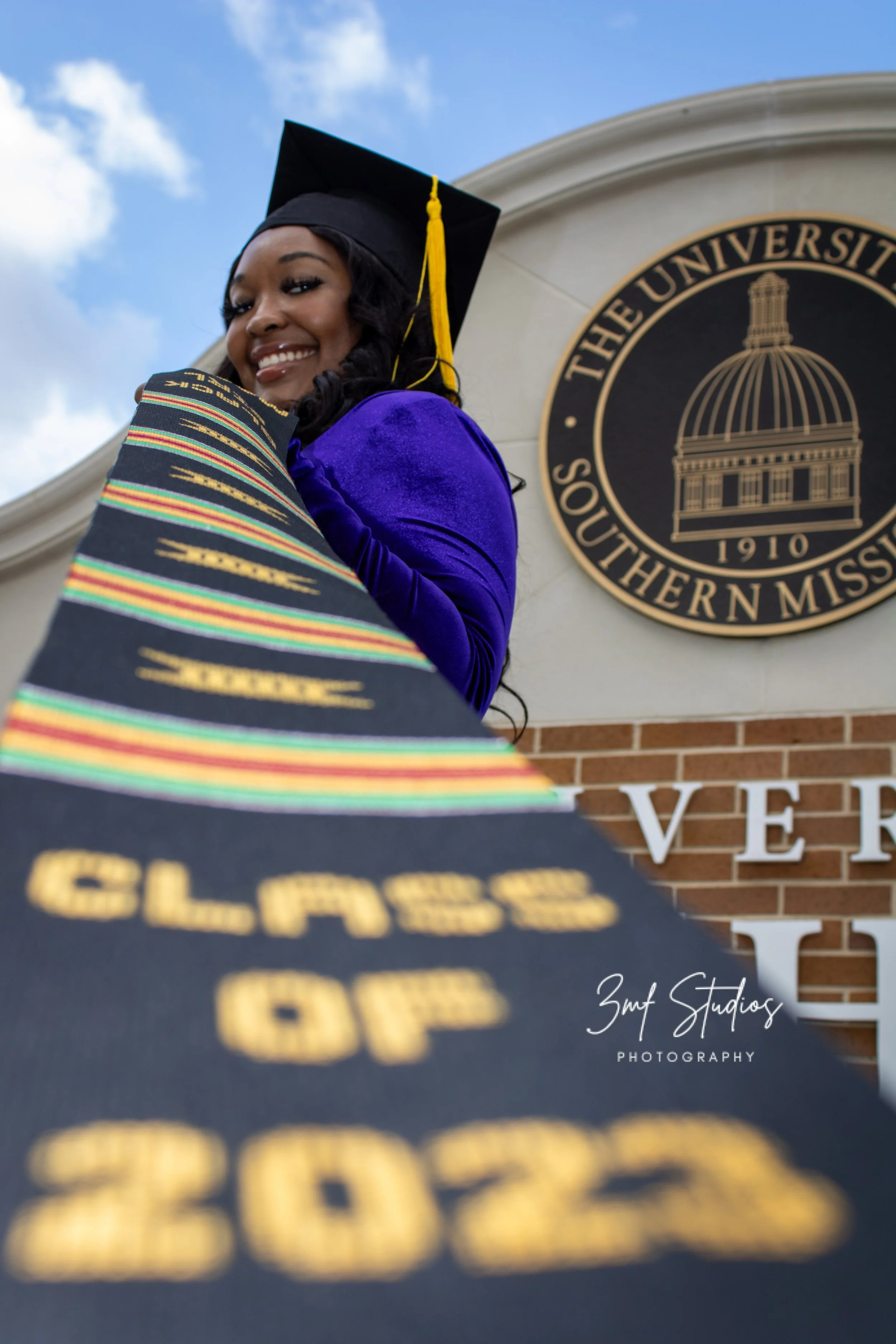 Graduating woman in cap and gown at university event with university emblem in background.