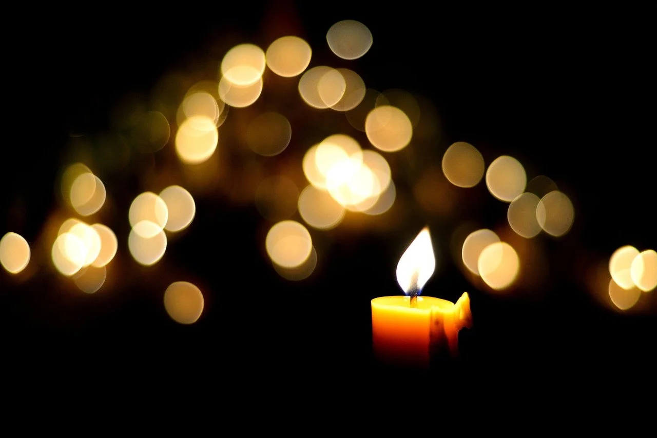 Une bougie allumée avec une flamme dans un environnement sombre, entourée de lumières floues en arrière-plan.