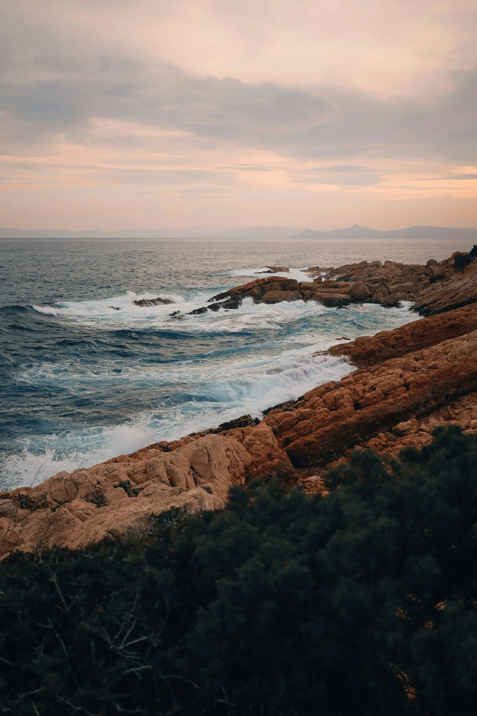 a beautiful coloured sunset with the waves hitting on the rocks in the Athenian Riviera