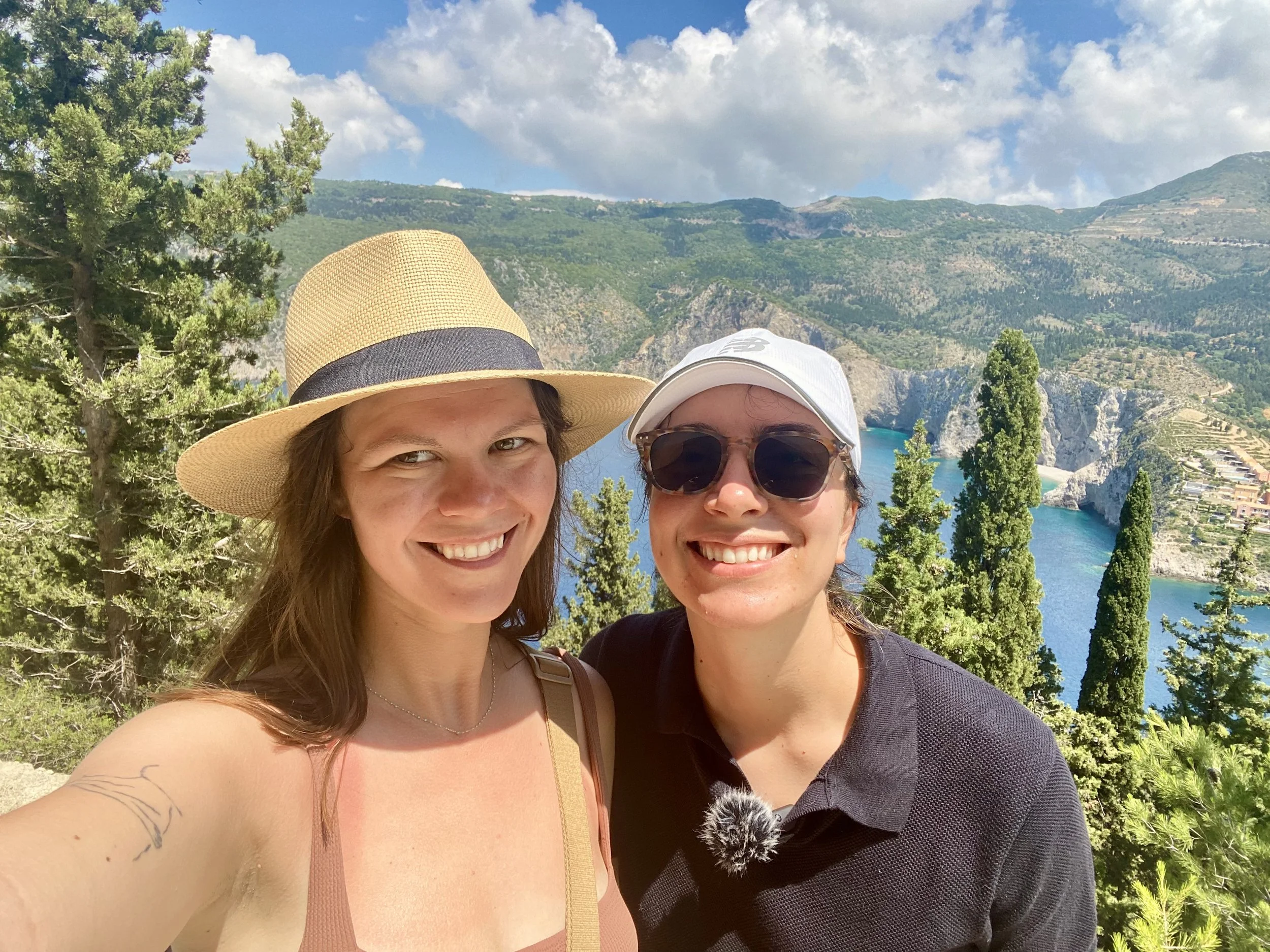 two women smiling at the top of a hill with Assos village kefalonia behind them