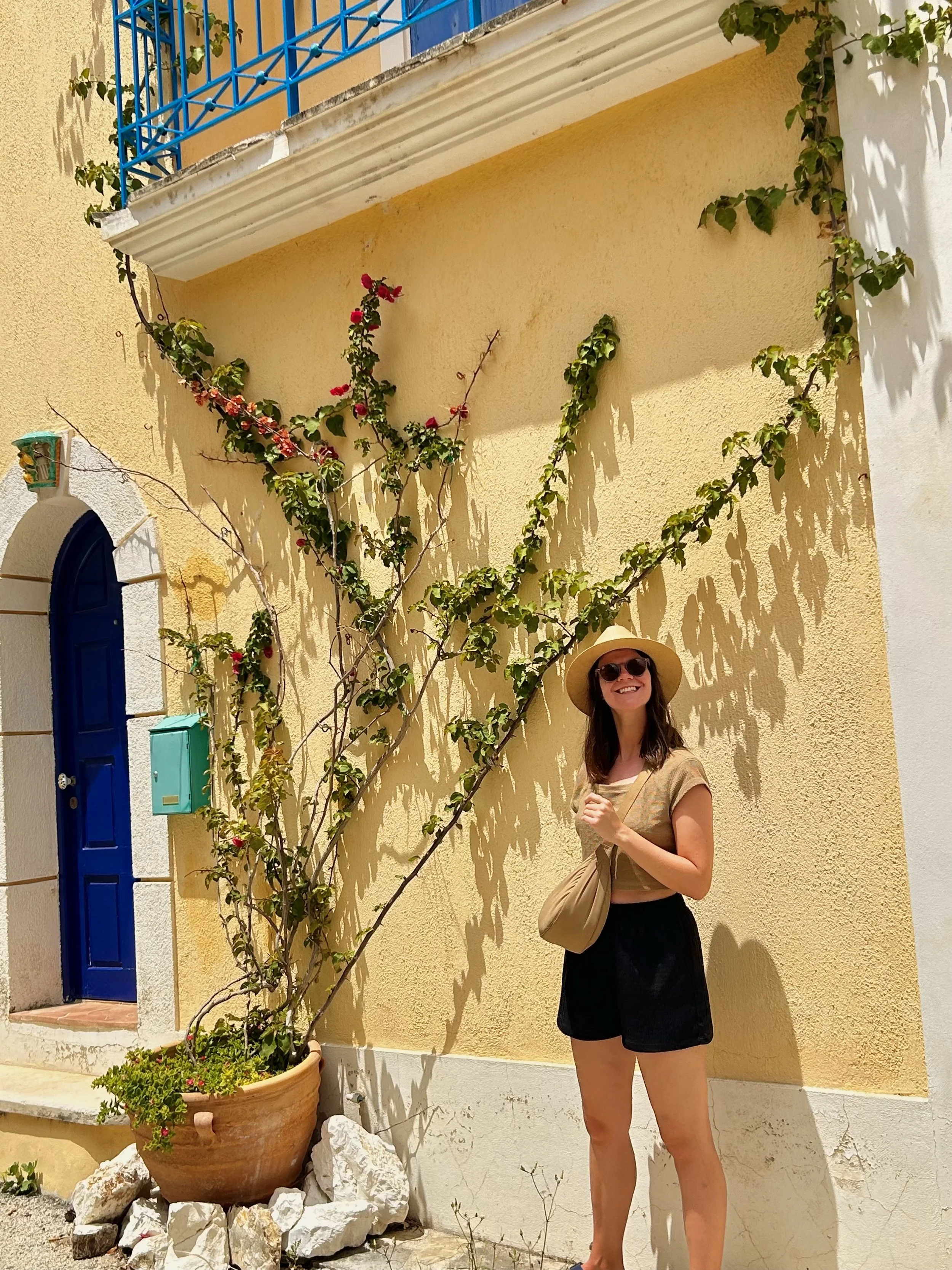 a girl smiling outside of a yellow building in Assos village, kefalonia island, greece
