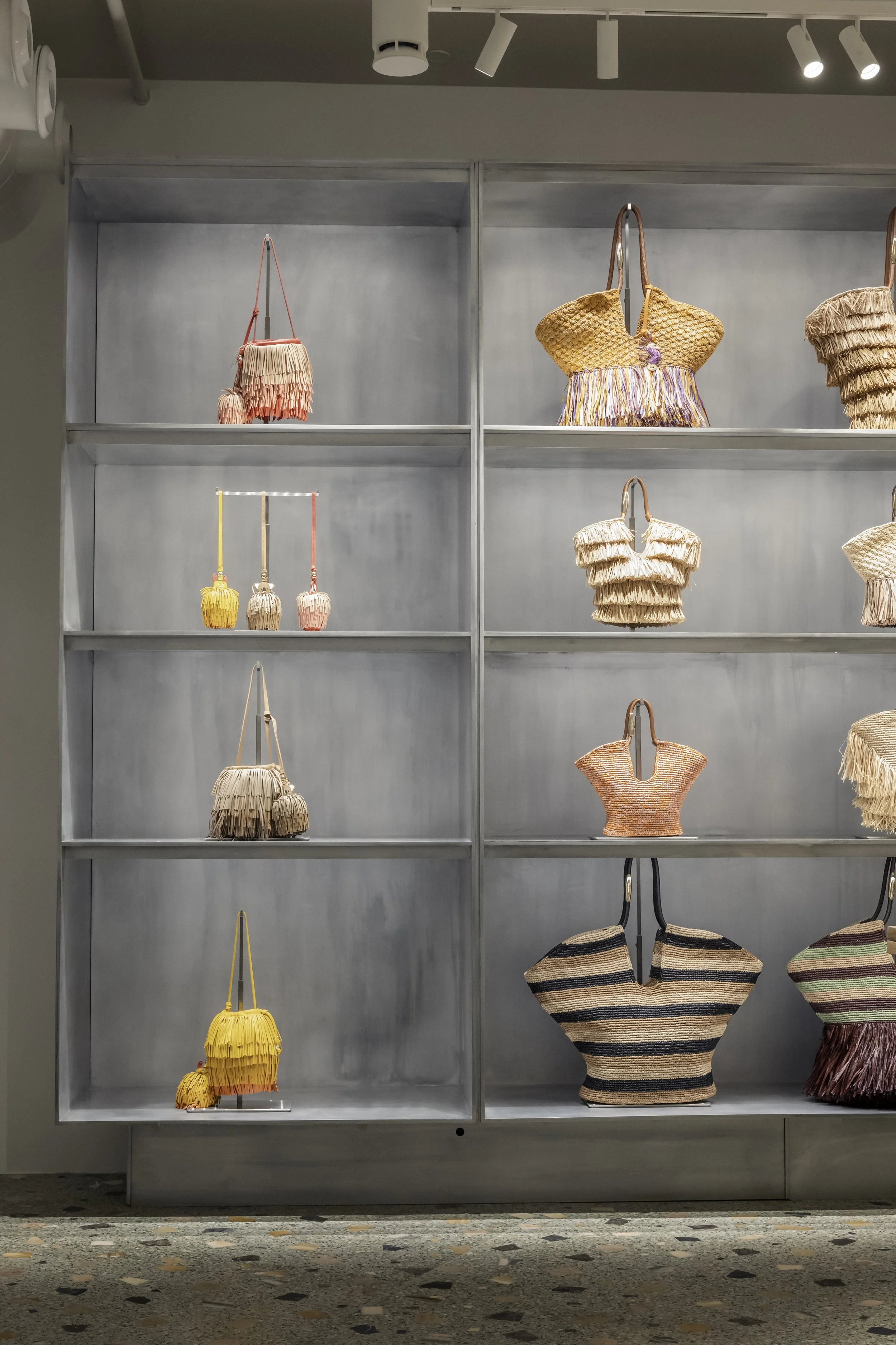 Display of colorful woven handbags and accessories on white shelves in a retail store.