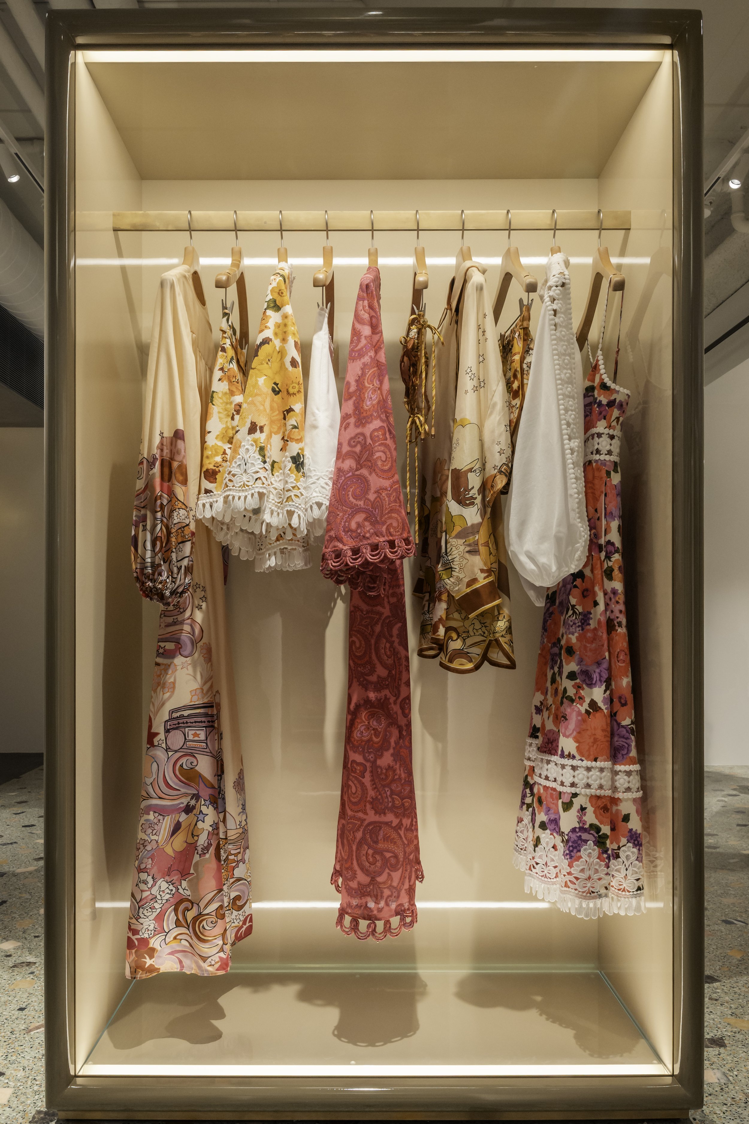A display case with several colorful, patterned dresses and skirts hanging on wooden hangers.