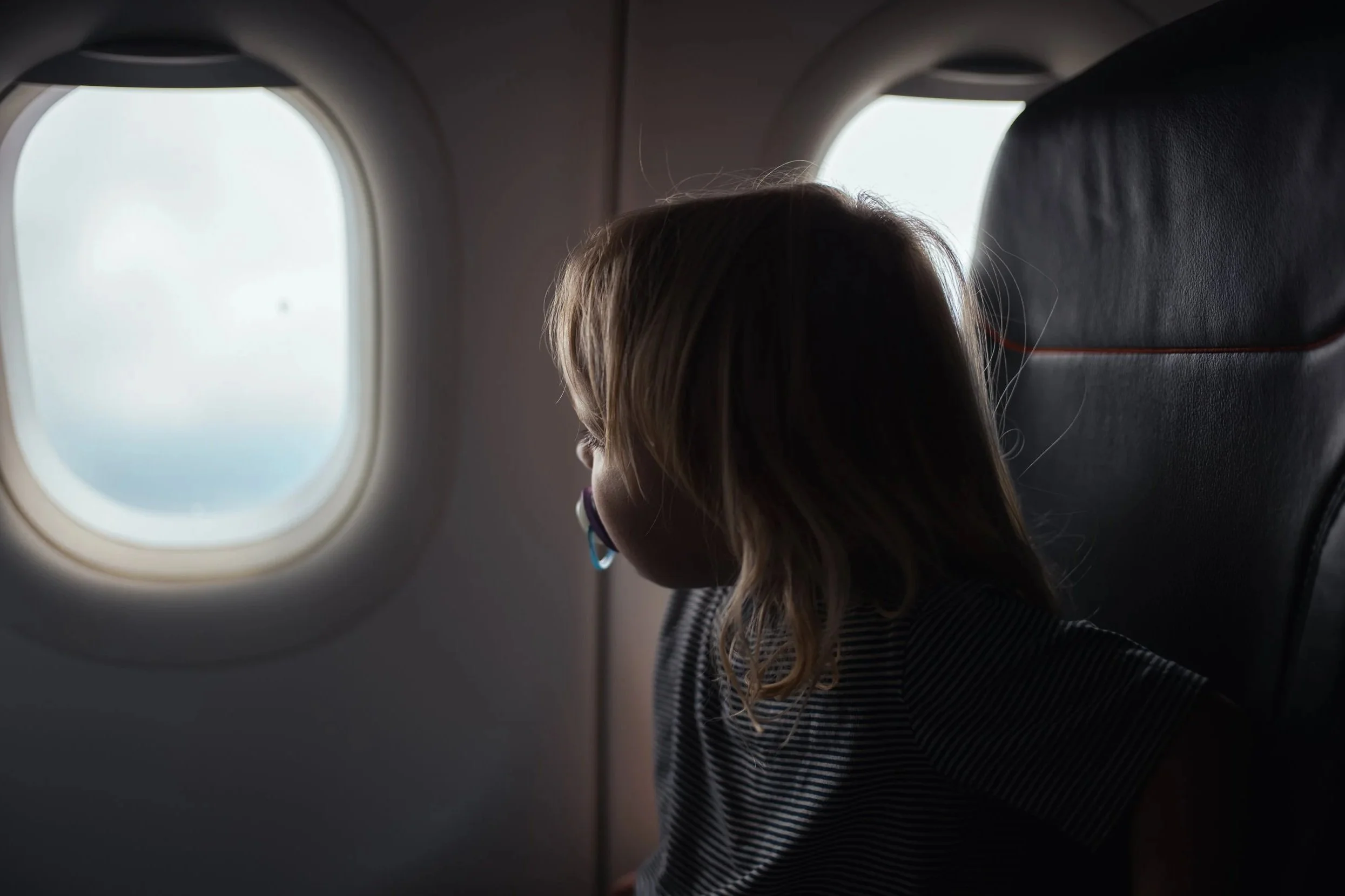 A young girl with blonde hair looking out of an airplane window.