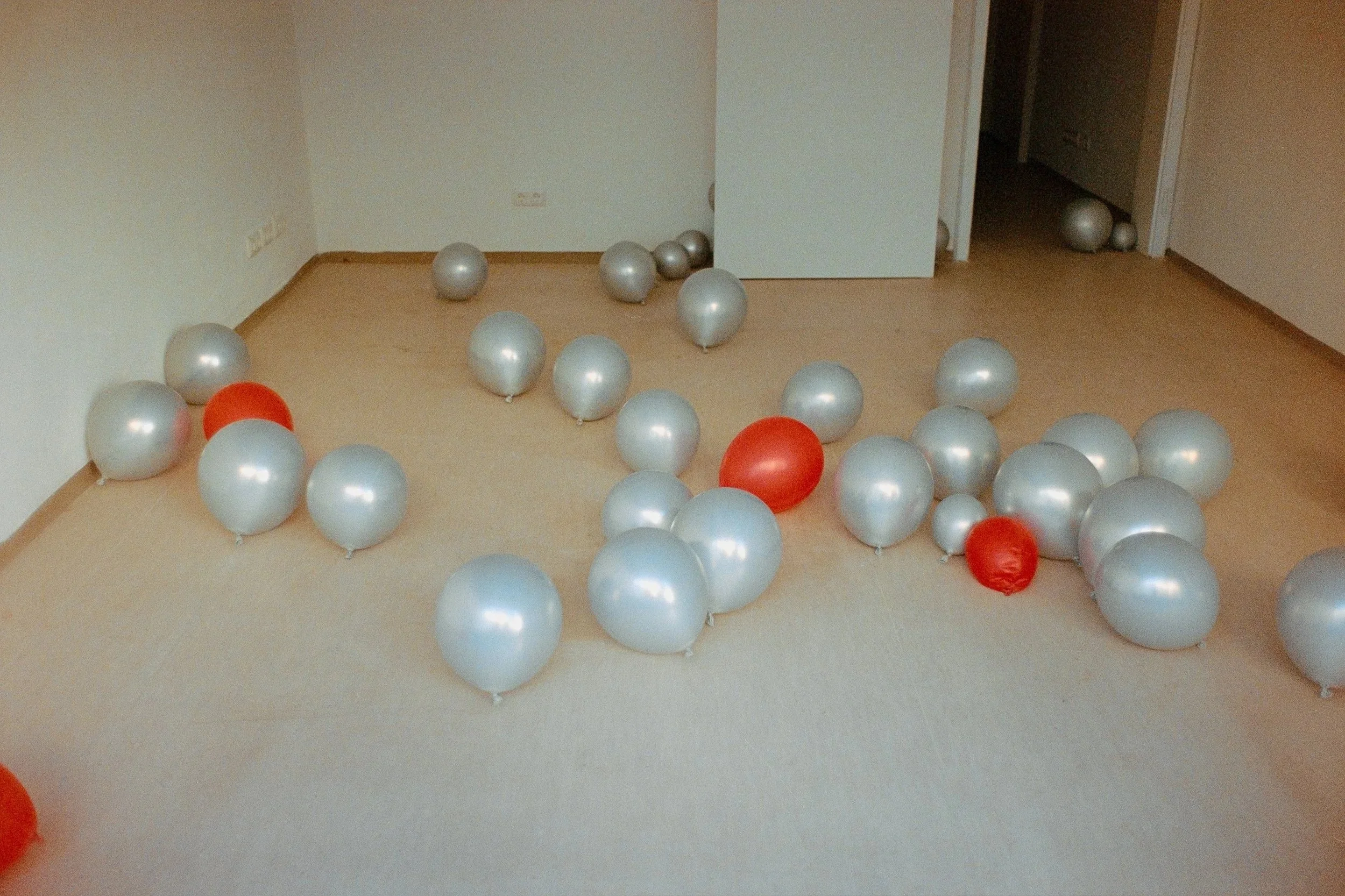 A room with a beige carpet and white walls filled with scattered silver and red balloons.