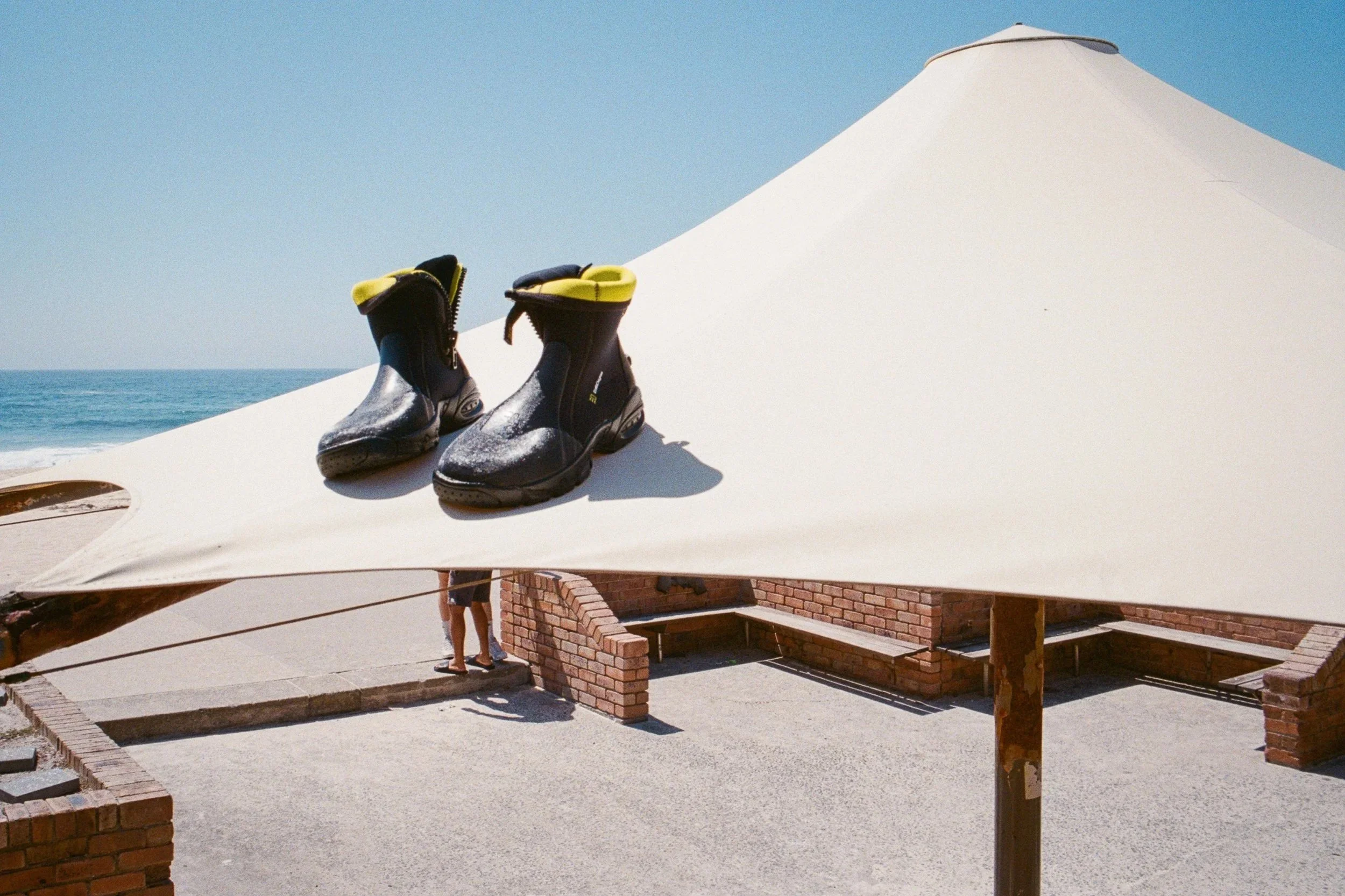 Black and yellow water shoes on a white beach umbrella at the beach with ocean and sky in the background.
