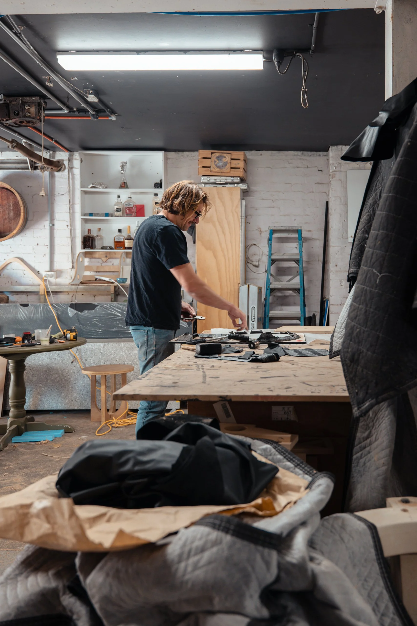 A man working on a woodworking project in a cluttered workshop with various tools, shelves, and materials around him.