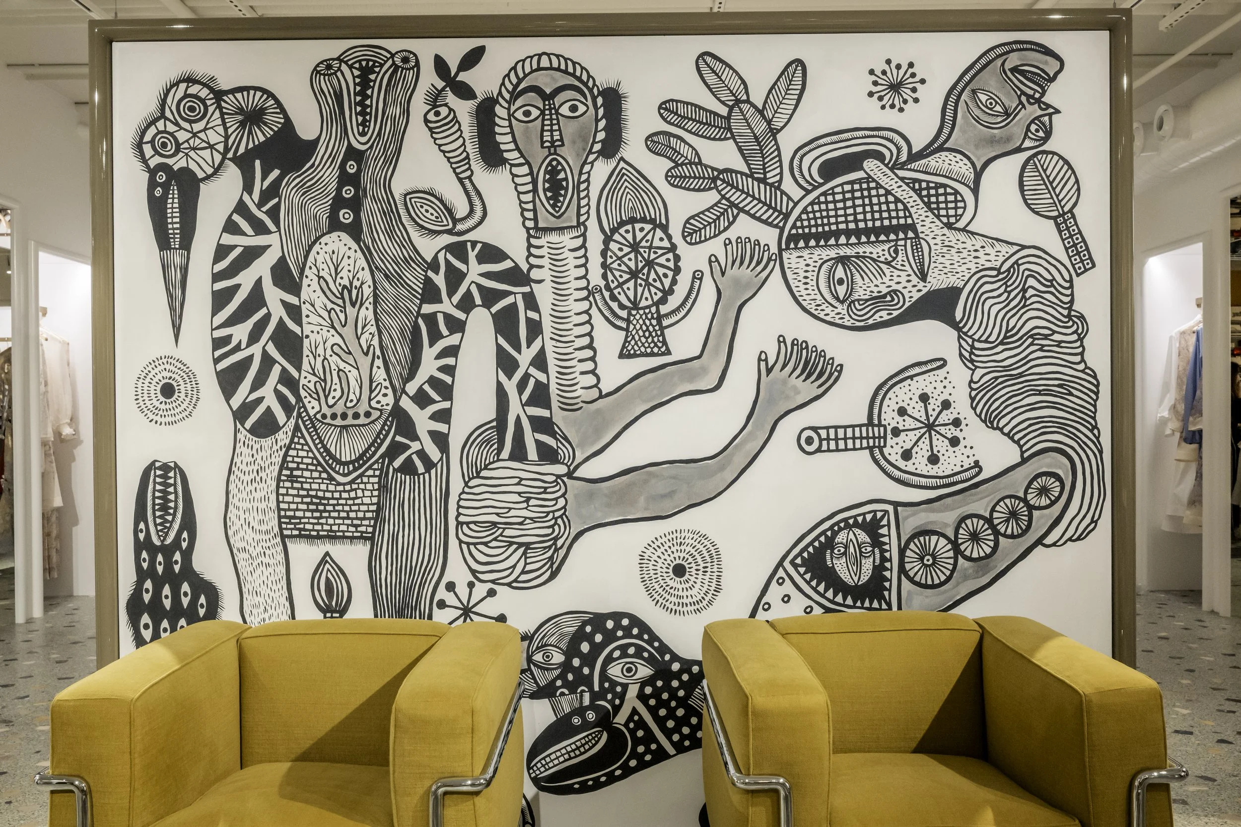Black and white mural with abstract and stylized animal and human figures, trees, and geometric shapes, with two yellow armchairs in front.