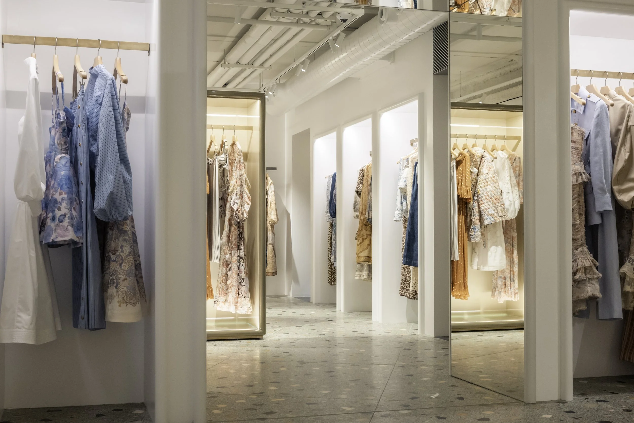 Clothing racks with pastel and floral dresses and tops in a modern boutique.