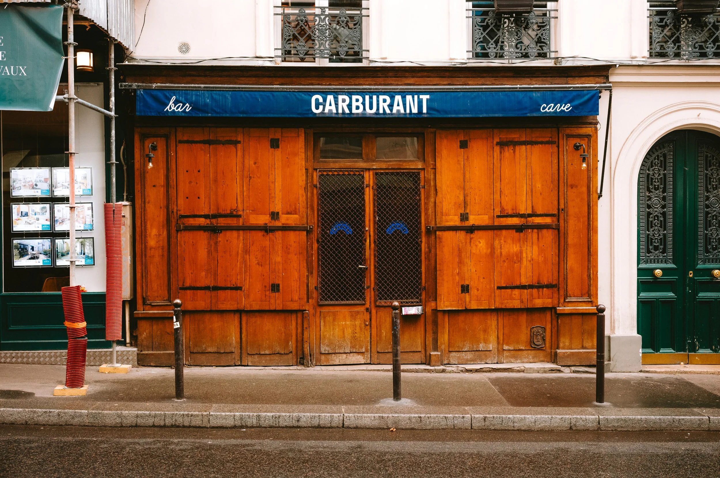 Closed wooden storefront with a blue sign that reads "bar" and "cave", and a large wooden door with wire mesh.