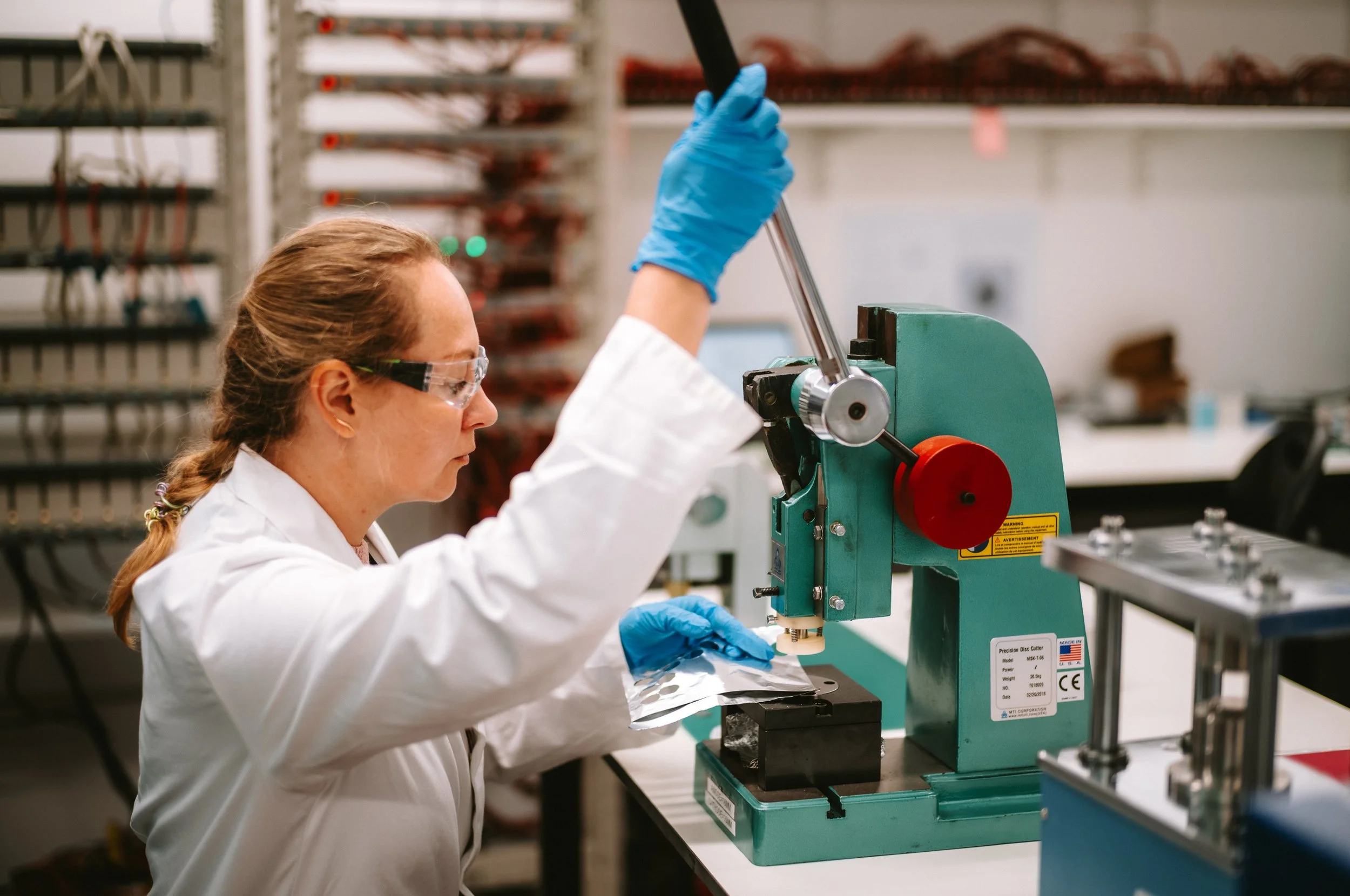 A scientist wearing safety glasses and blue gloves operating a scientific machine in a laboratory.