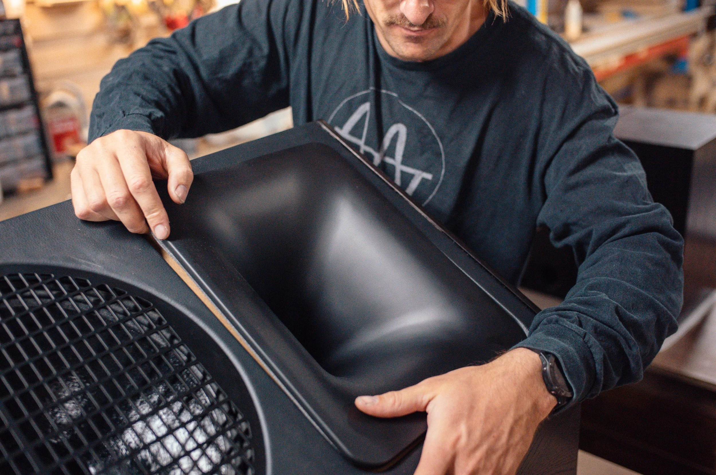 A person is lifting a black speaker, revealing a built-in handle and grille.