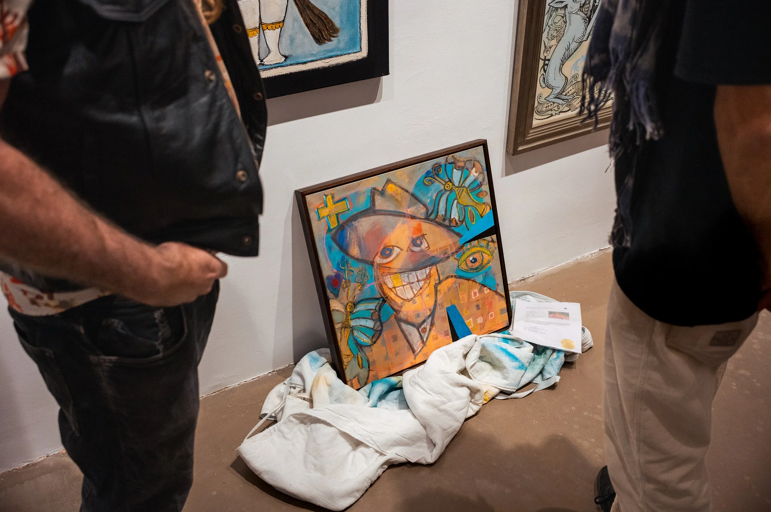 Two people standing around a colorful abstract painting of a smiling person with a hat in an art gallery