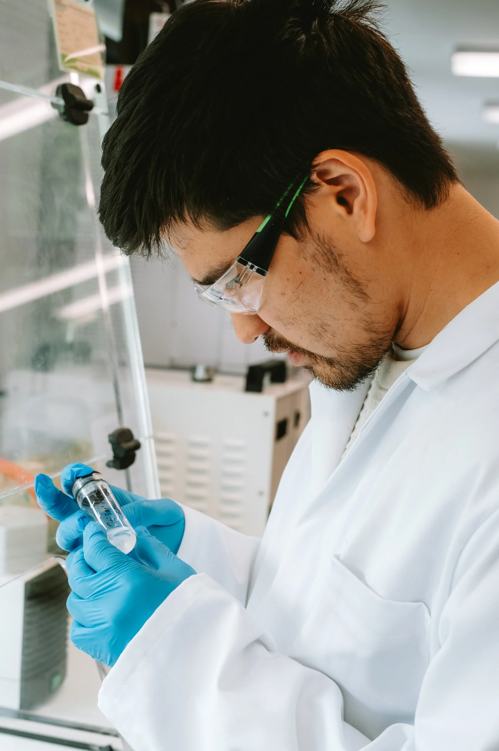 A scientist in protective glasses and blue gloves examining a test tube in a laboratory.