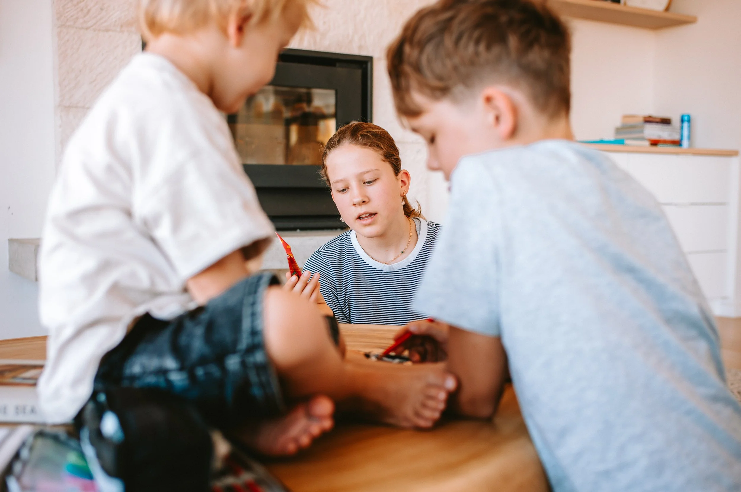 Three children playing a game on a wooden table in a cozy living room.