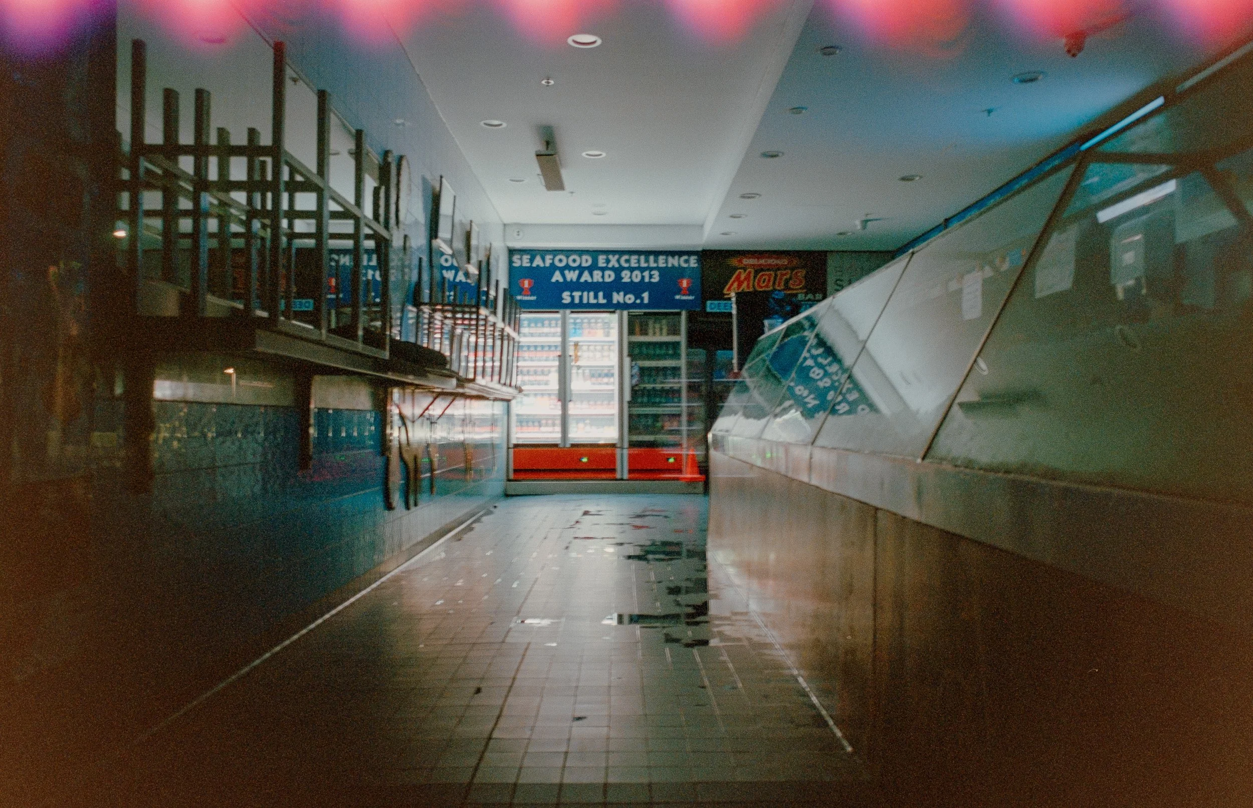 Empty convenience store aisle with a sign recognizing seafood excellence award in 2013 and vending machines in the background.