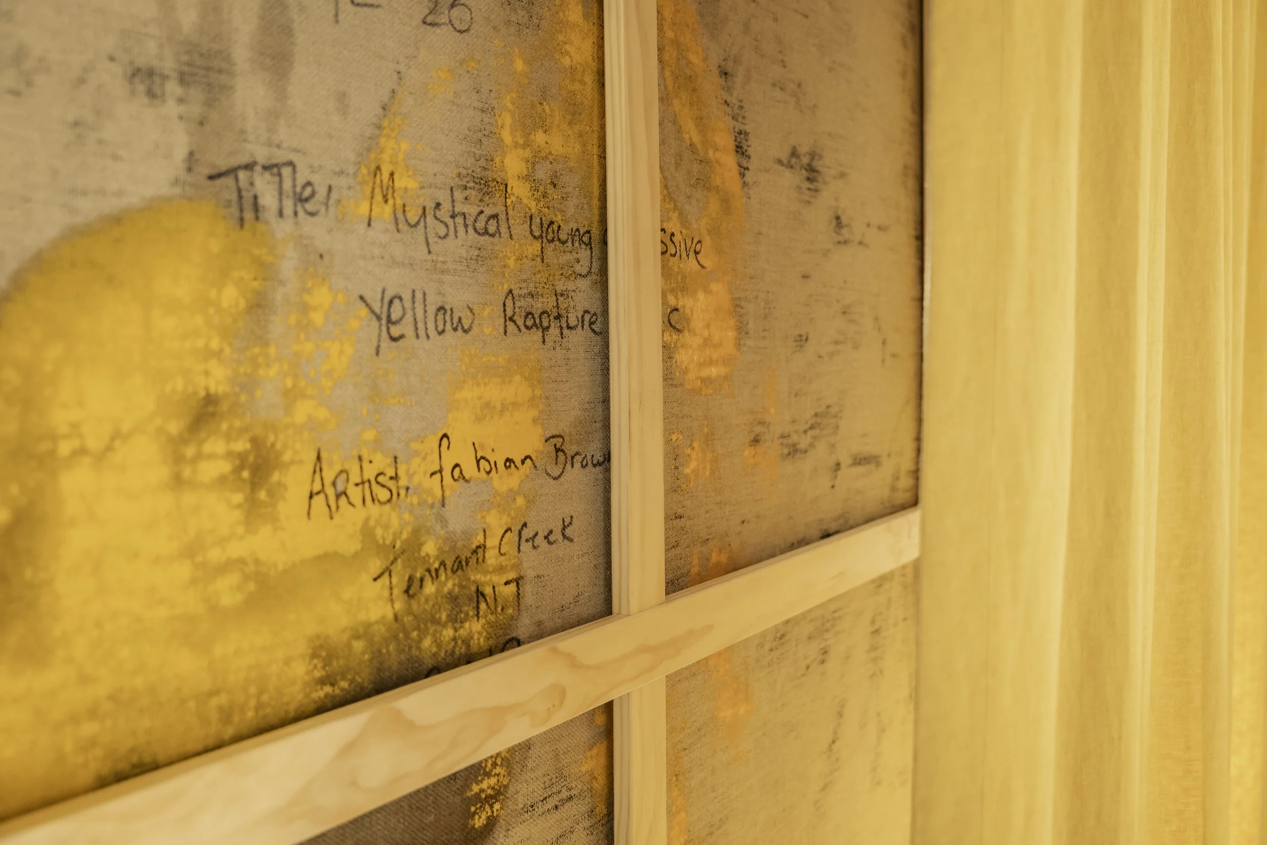 Close-up of a textured wall or canvas with handwritten text, including the words "The Mystical Young" and "Yellow" among others, framed with wooden strips on the right side.