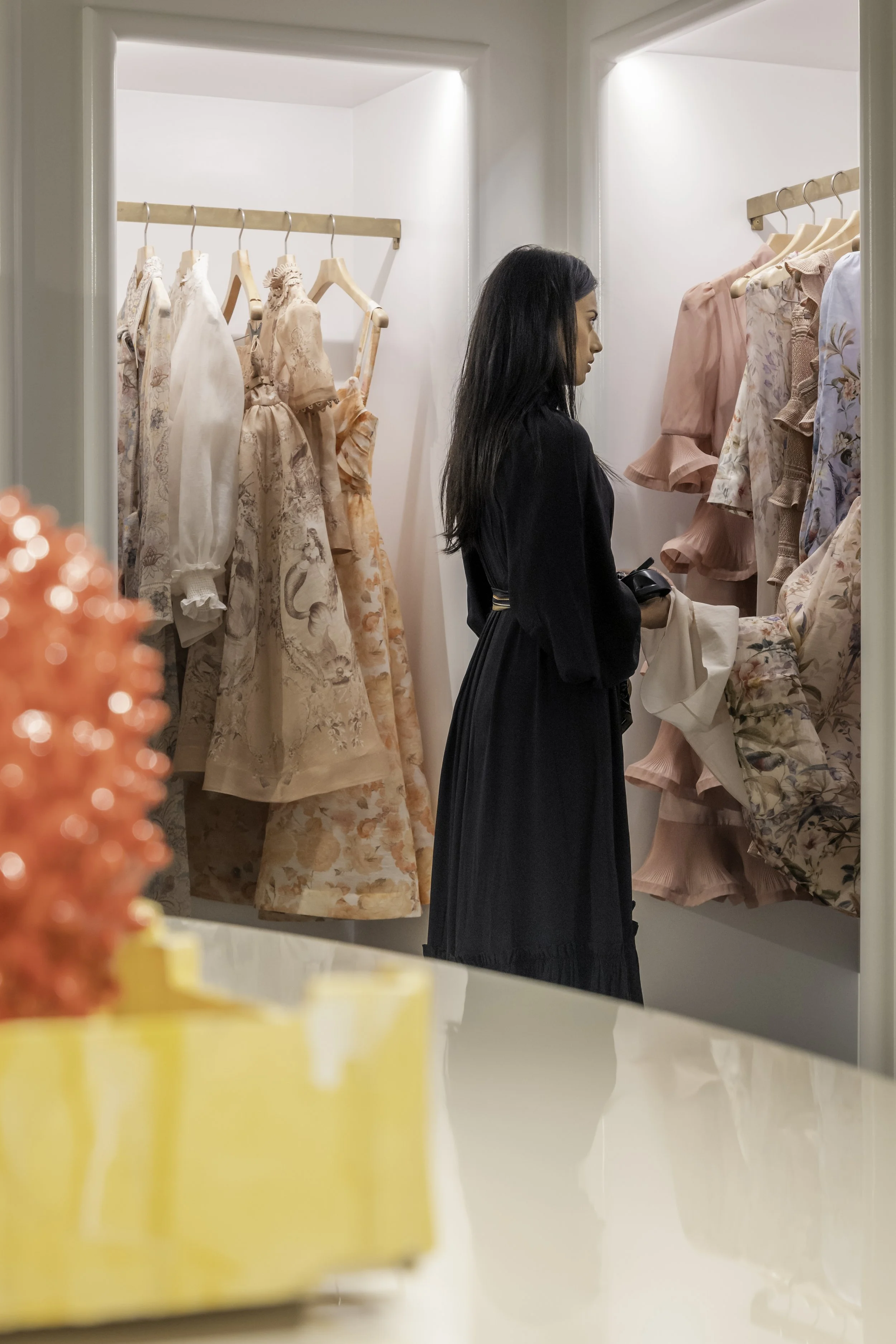 A woman shopping for pink and floral dresses in a boutique dressing room.
