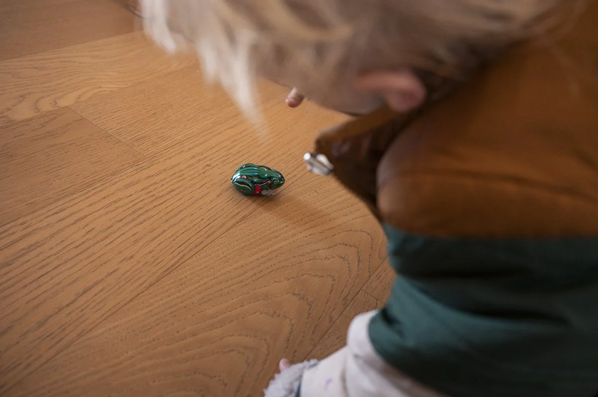 A child sitting at a wooden table looking at a small, colorful, decorative object on the table.