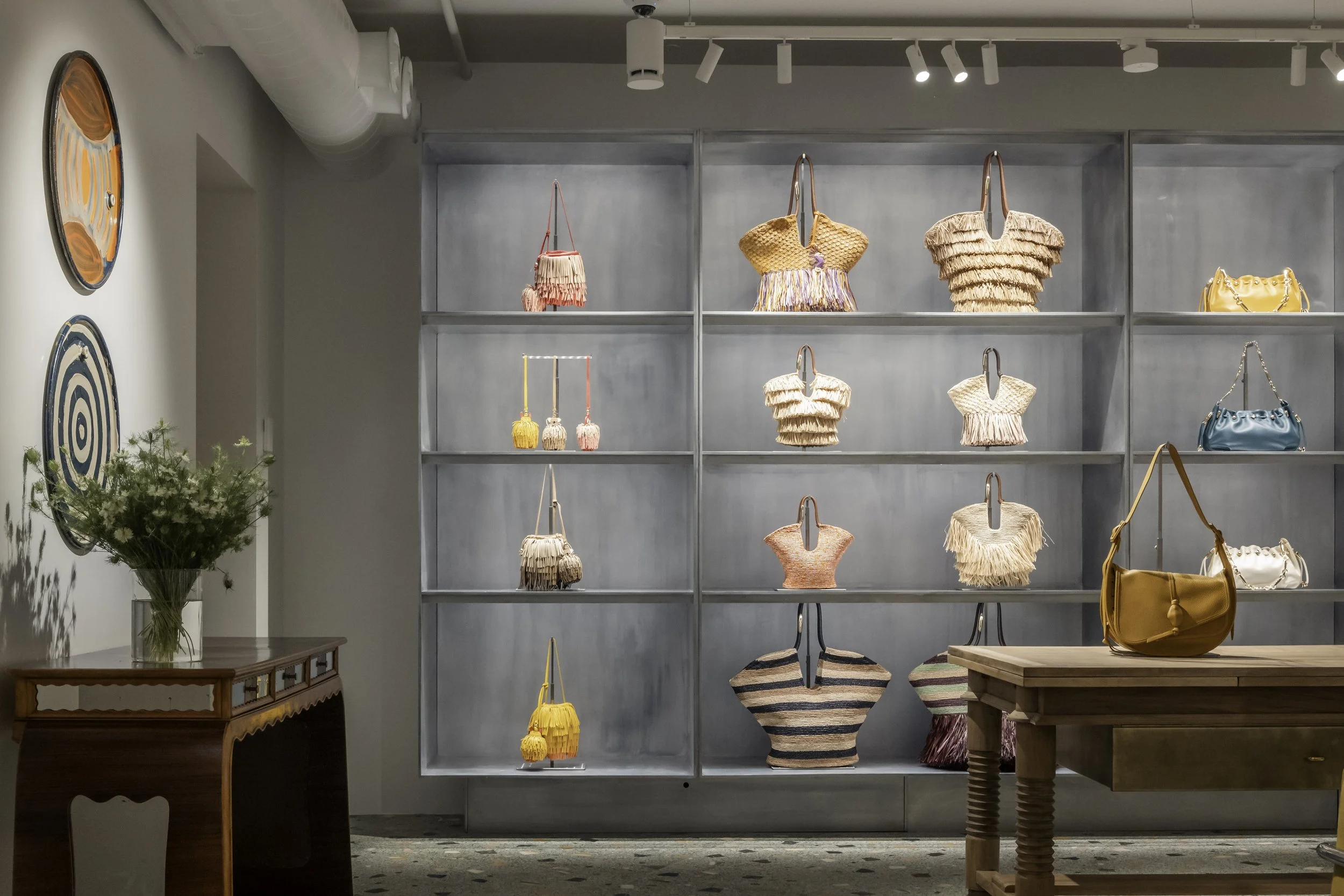Display of colorful handbags and purses on a metal and glass shelf in a retail store.