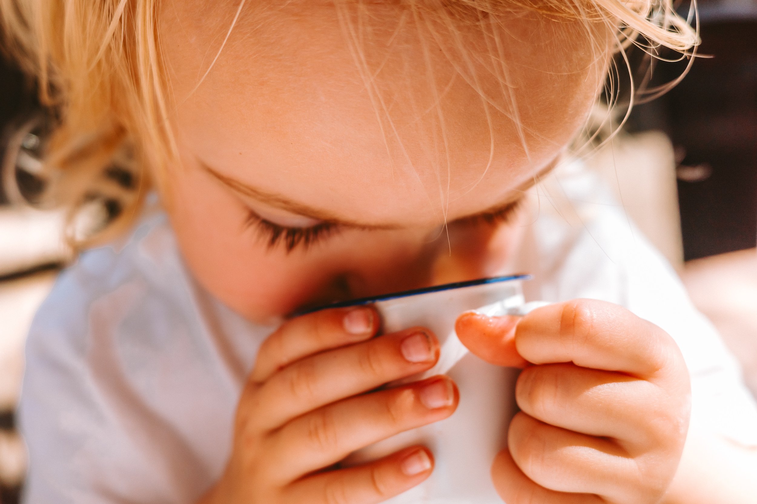 A young girl with light hair drinking from a white mug.