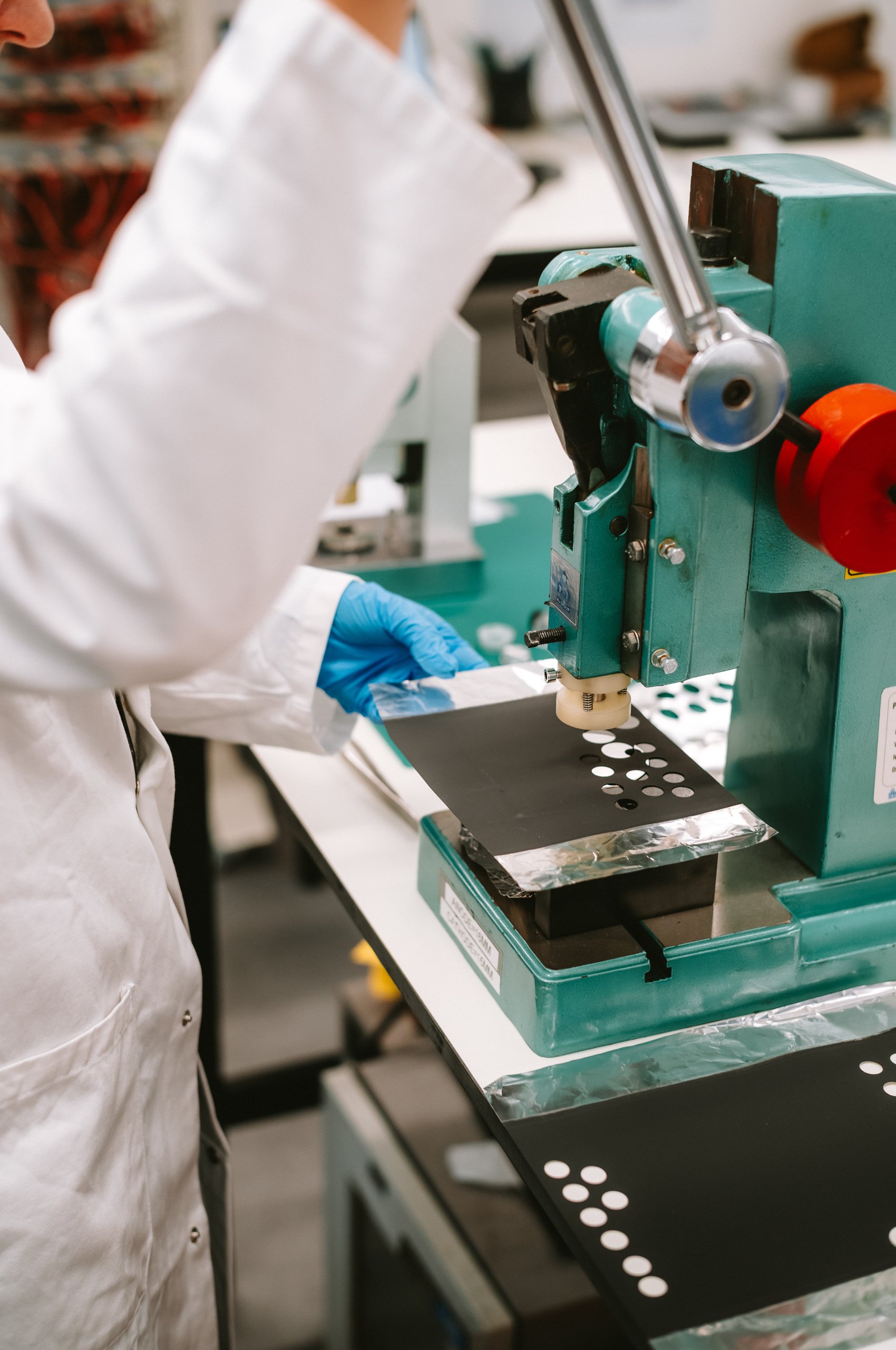 Laboratory technician in a white coat and blue gloves operating a microchip manufacturing machine in a lab.
