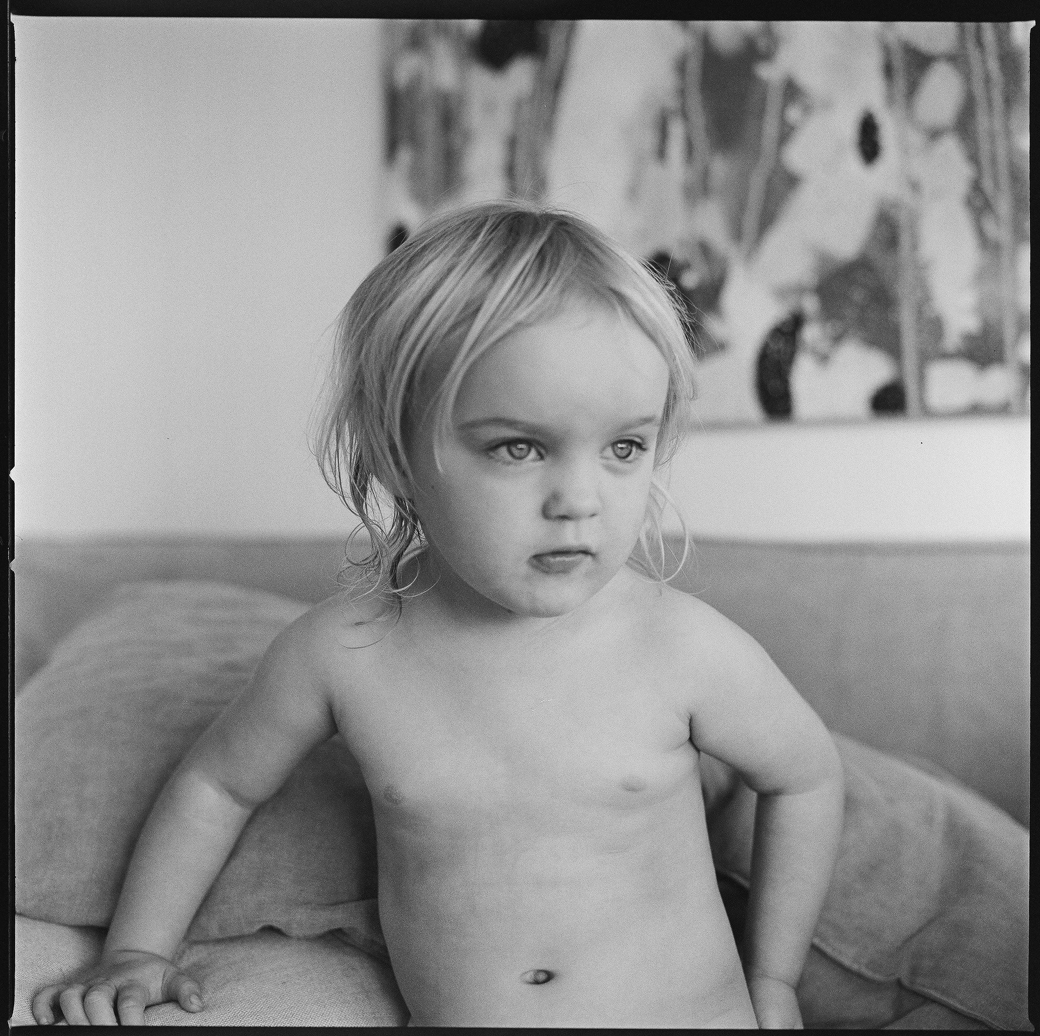 Black and white photo of a young girl with wet hair, sitting on a couch with her hands resting behind her.
