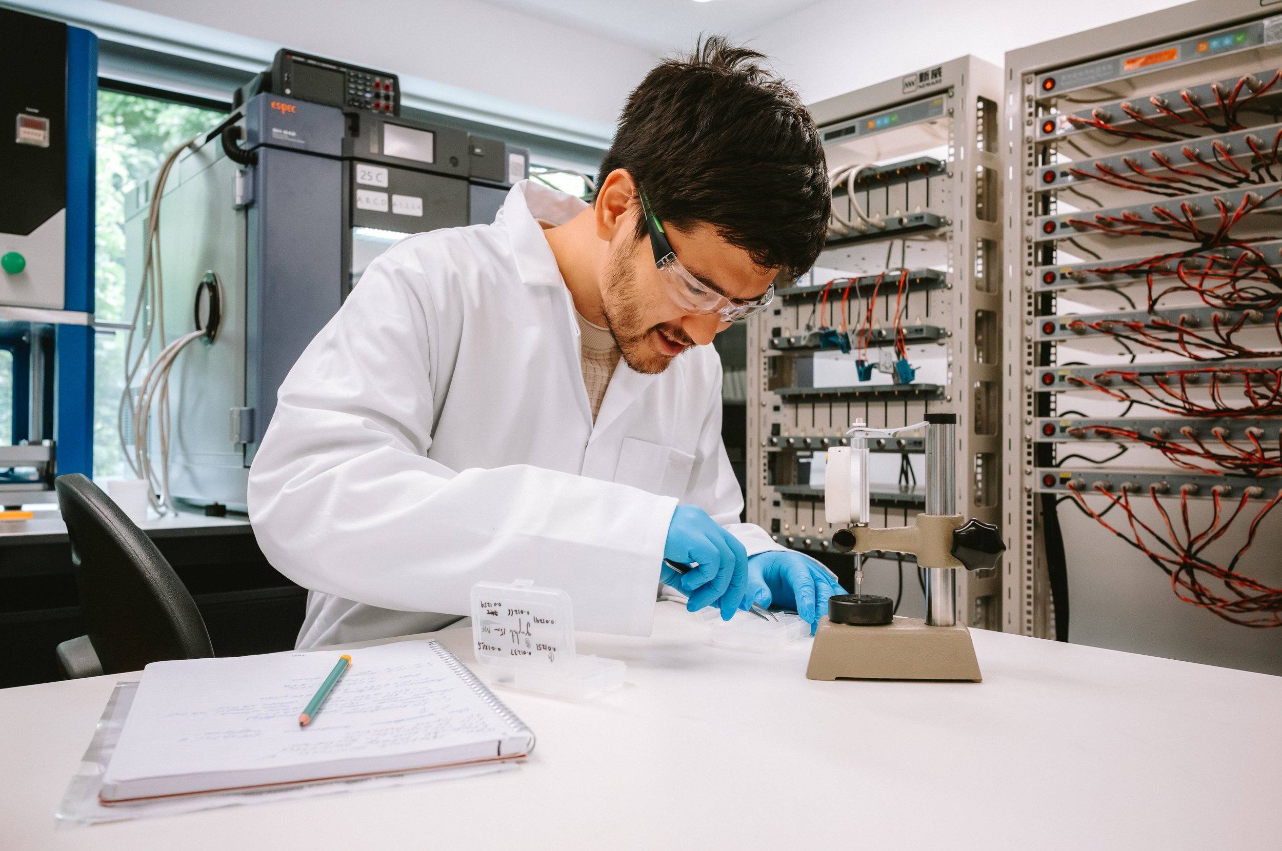 A scientist in a white lab coat and safety goggles working with laboratory equipment in a lab.