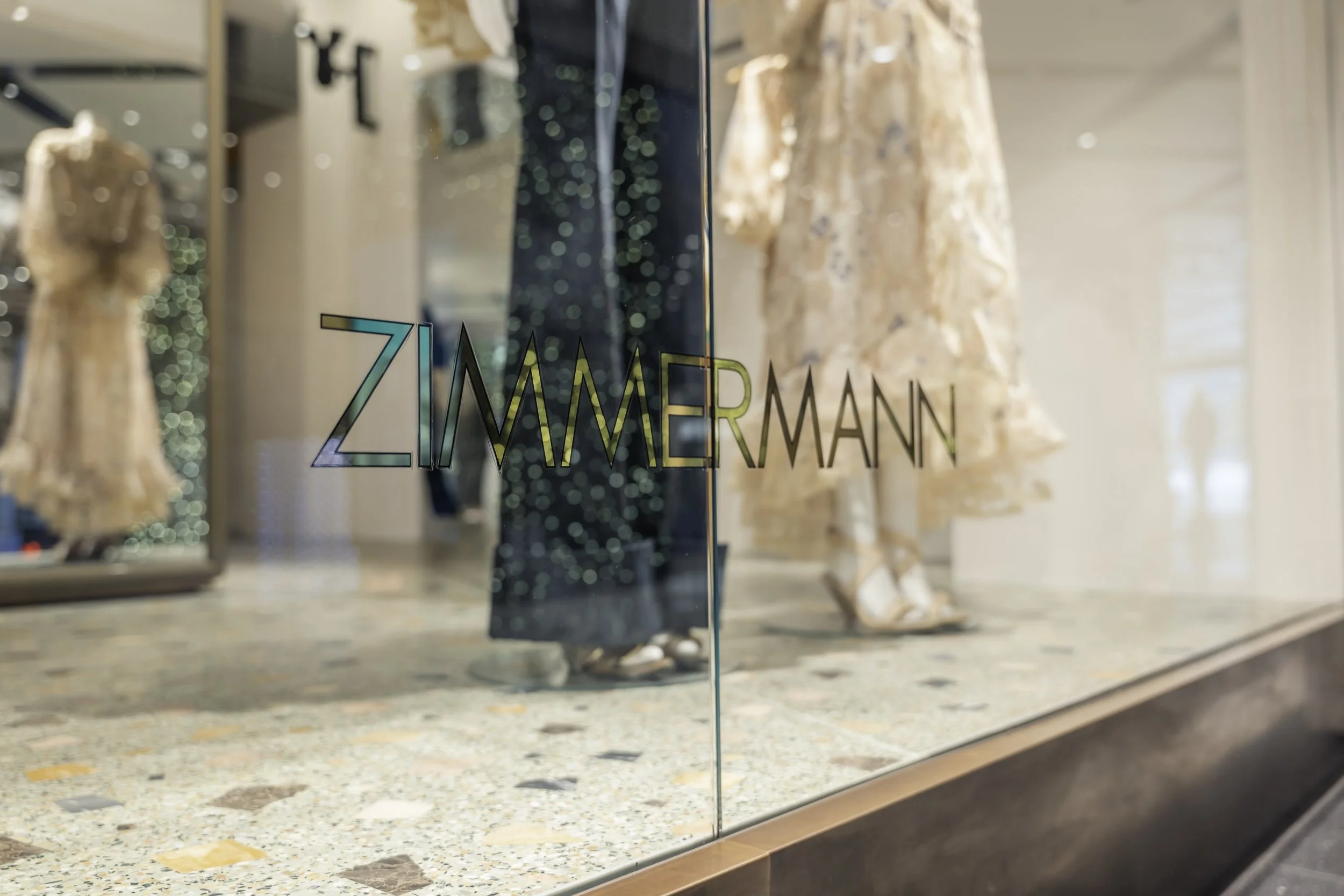 Store window with the text "ZIMMERMANN" on the glass, displaying mannequins dressed in elegant clothing inside.