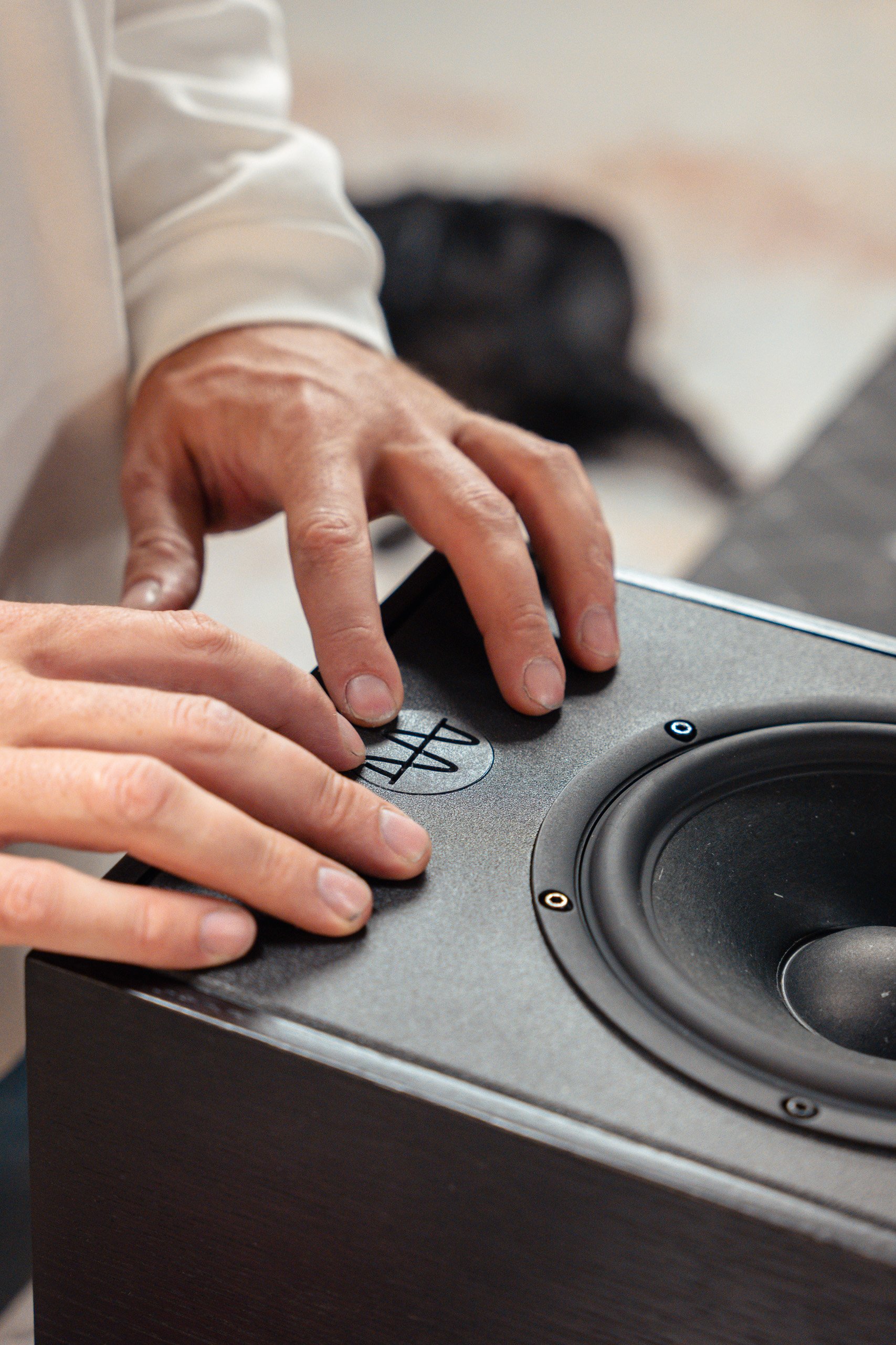 Close-up of a person's hands adjusting the control on a speaker speaker with visible speaker cone, in a room with blurred background.
