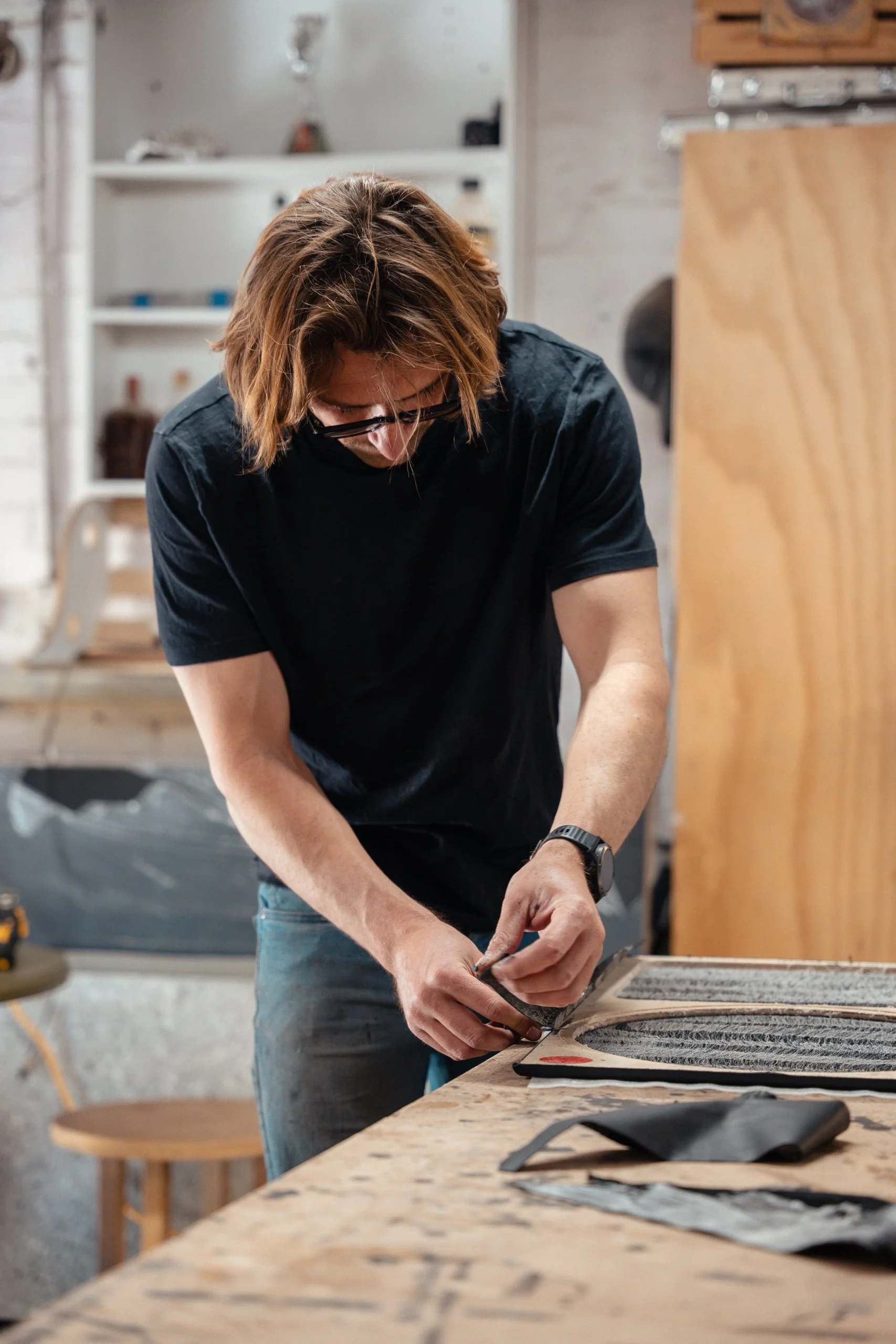 Man working on a craft project at a wooden workbench in a workshop.
