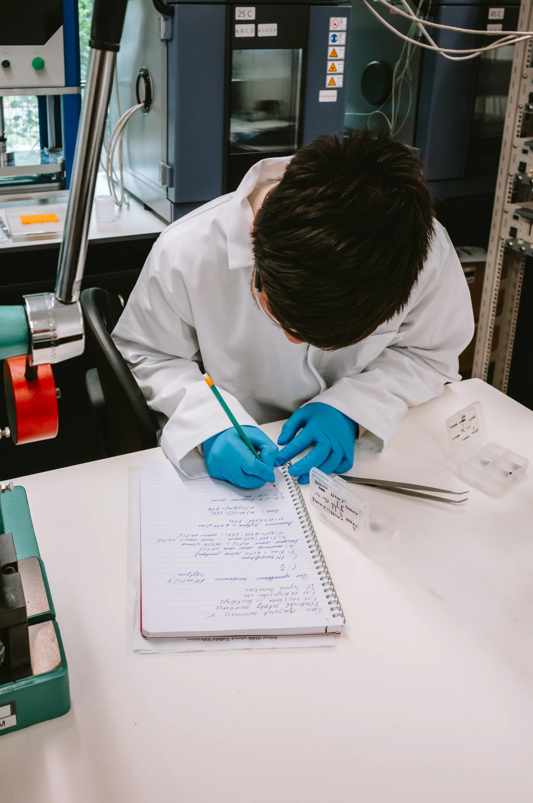 A scientist in a laboratory writing in a notebook while wearing blue gloves and a white lab coat.
