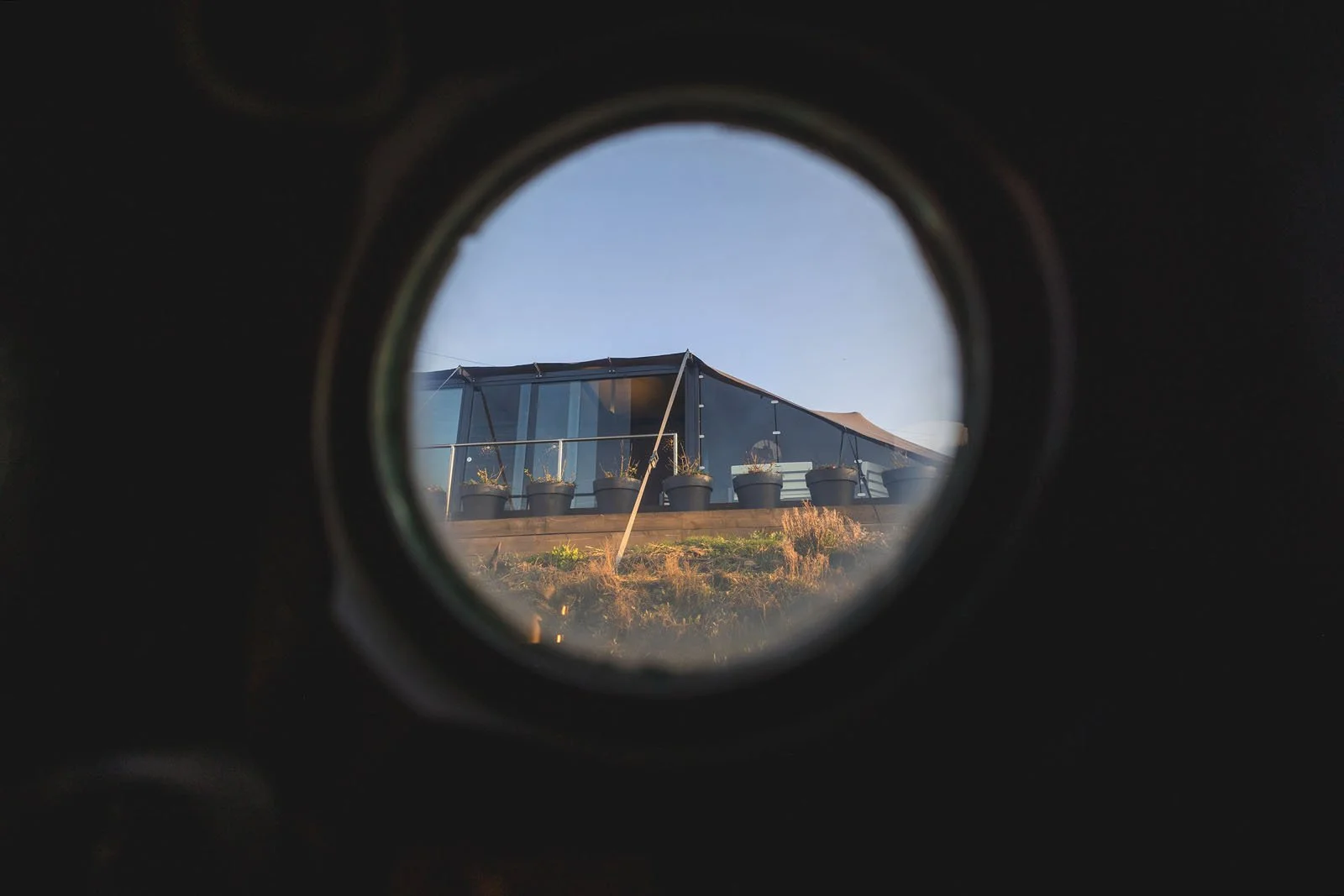 View of a modern glass building with a rooftop terrace through a circular opening.