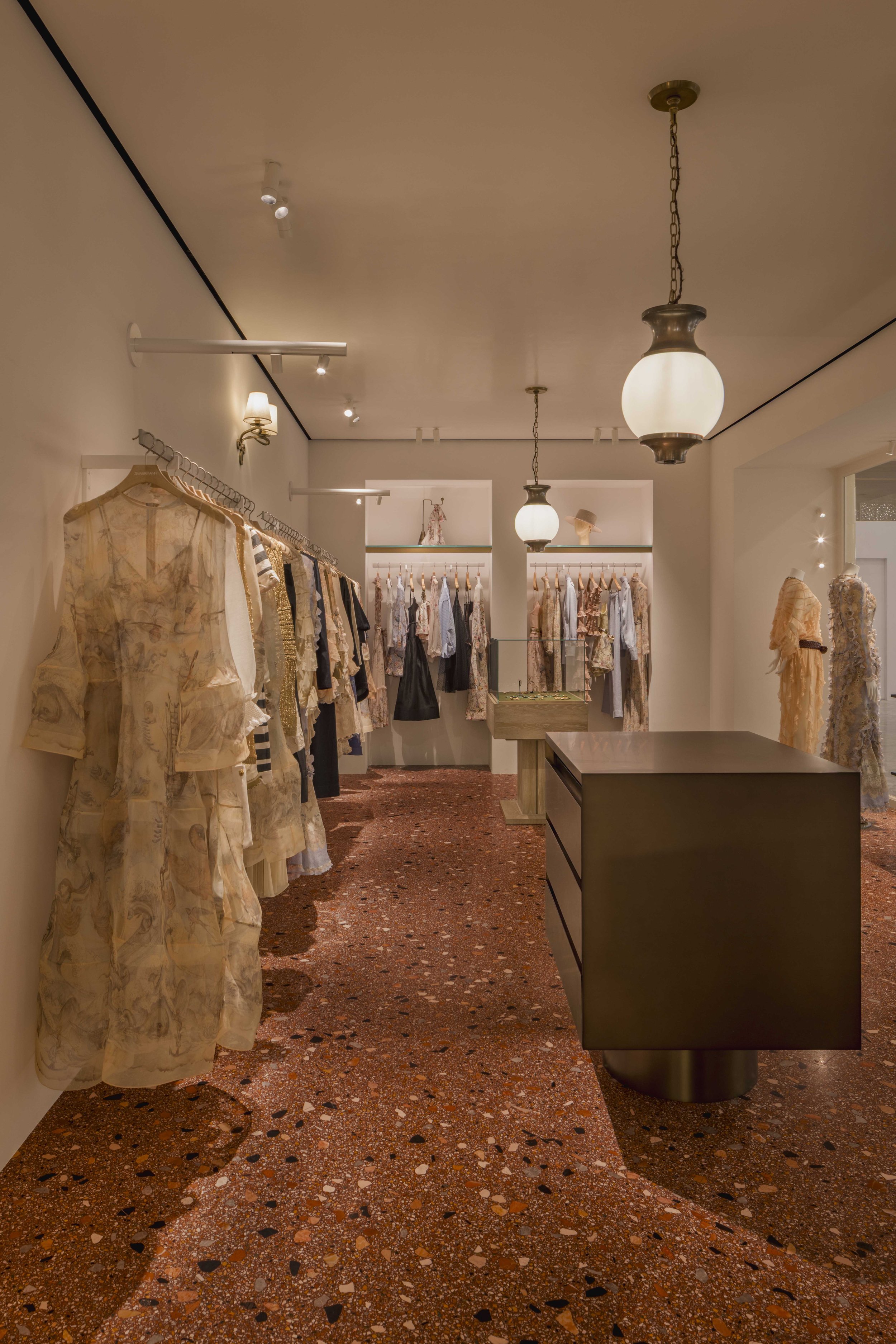 Inside a boutique clothing store with racks of clothing on both sides and hanging lantern lights from the ceiling.