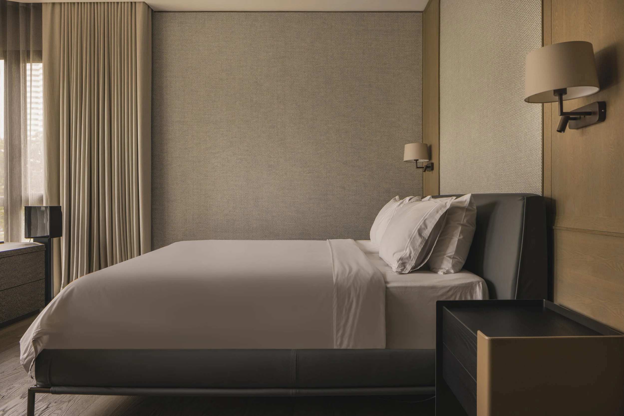 A modern hotel room with a bed, bedside lamps, and a window with curtains.