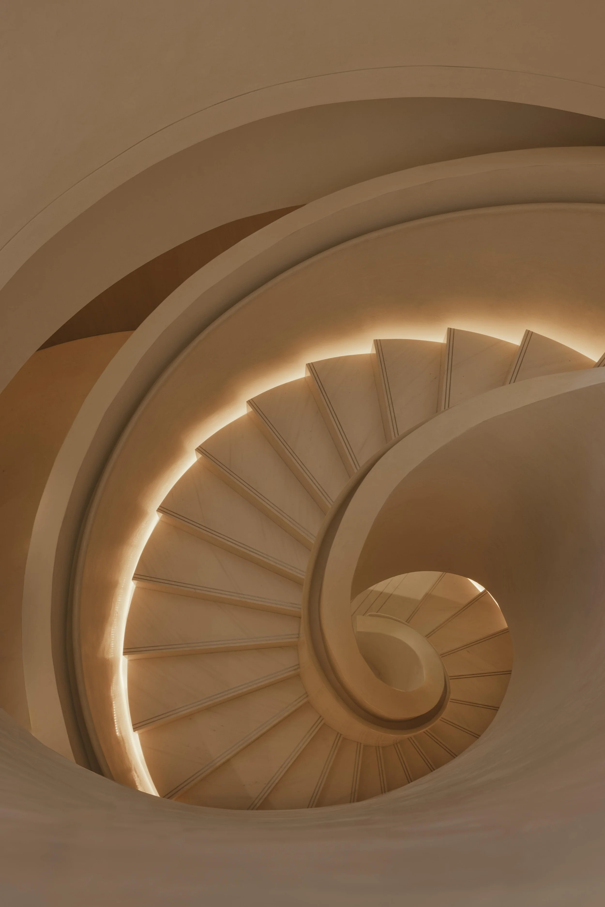Interior view of a spiral staircase with warm lighting highlighting its curves and steps.