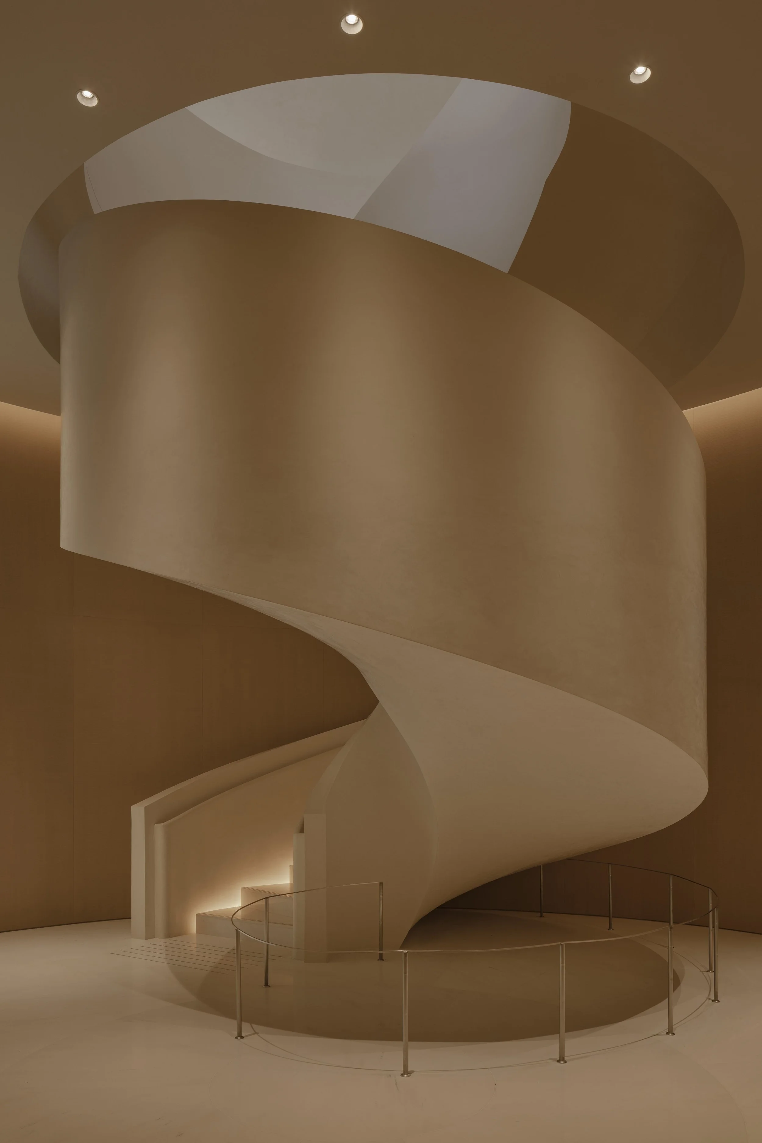 Interior view of a modern, abstract staircase with a swirling, spiraling design, beige and white color tones, and small metal railing around the perimeter.